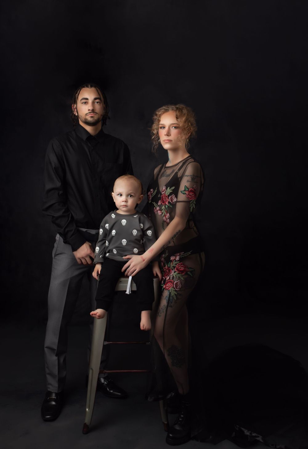 Family of three posing together against dark studio backdrop.