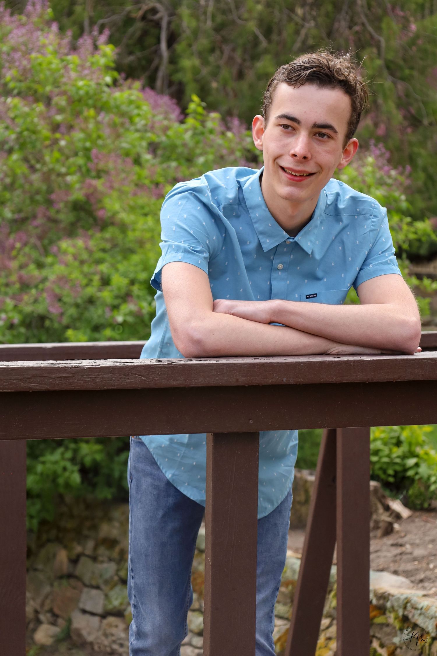 Casual portrait on a wooden deck railing with purple flowers in the background.