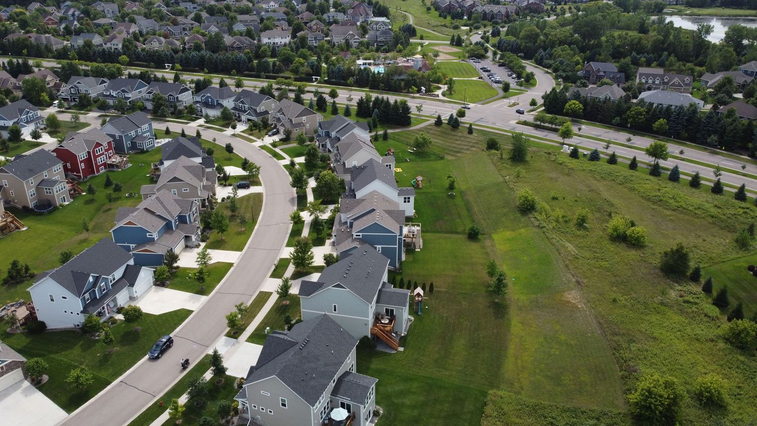 Aerial view of residential neighborhood with curved streets and gray houses surrounded by green space.