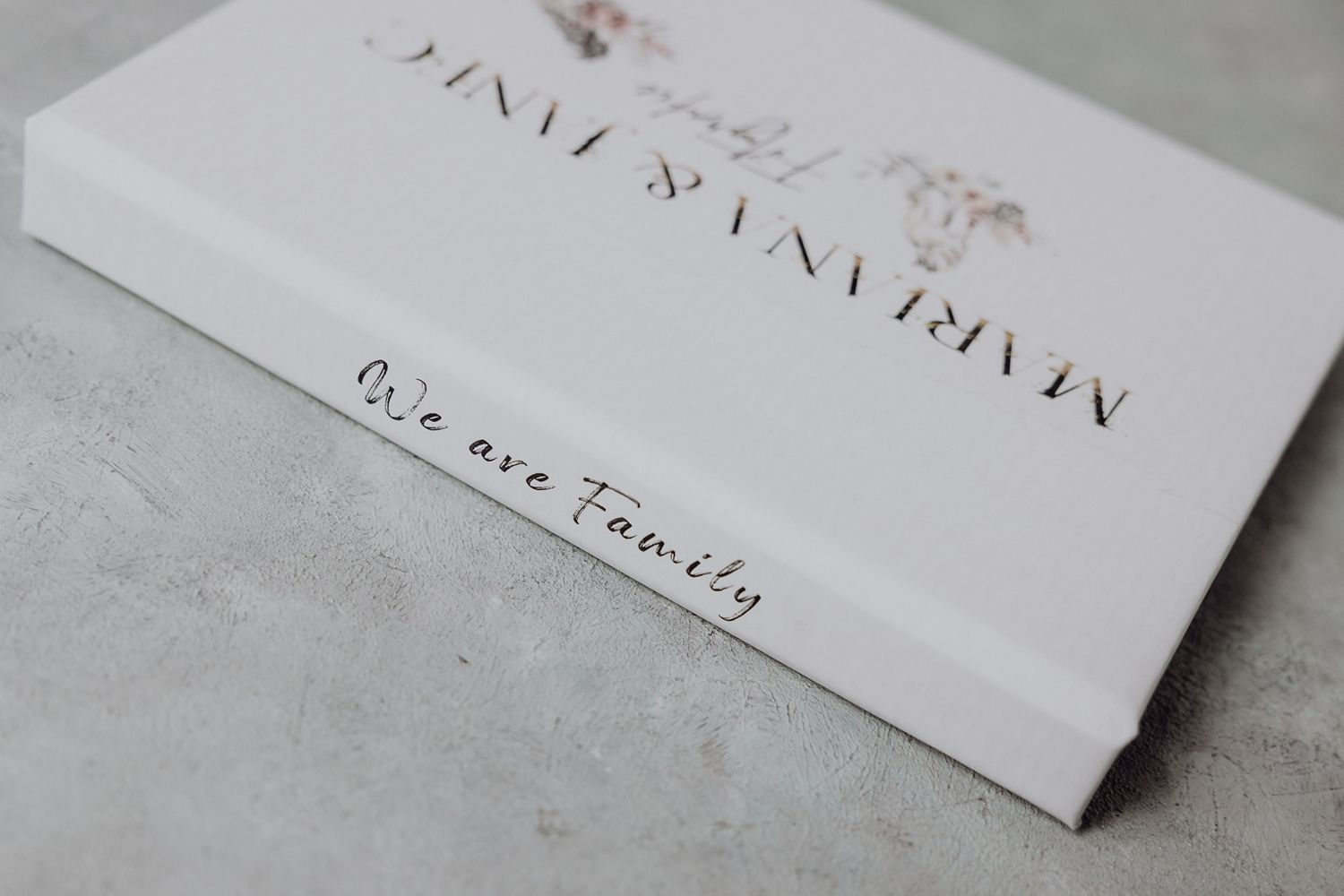 White photo album cover with elegant gold text design on concrete surface.