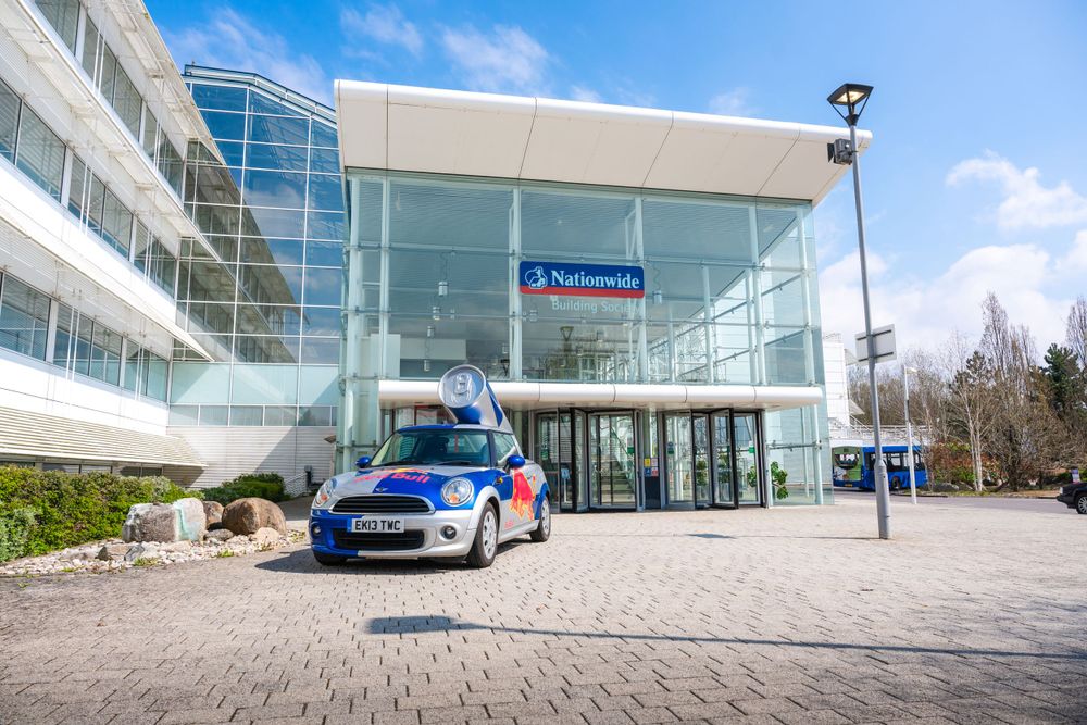 Modern office building exterior with a blue Mini Cooper parked in front.