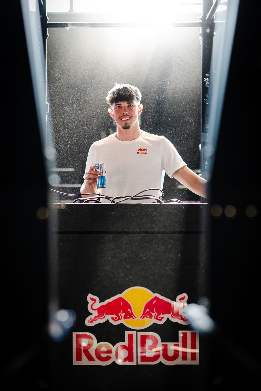 DJ performing behind a Red Bull branded booth in dramatic lighting.