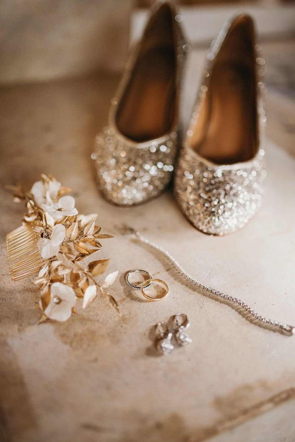 Sparkly wedding flats with jewelry accessories and floral hairpiece arranged on a light surface.