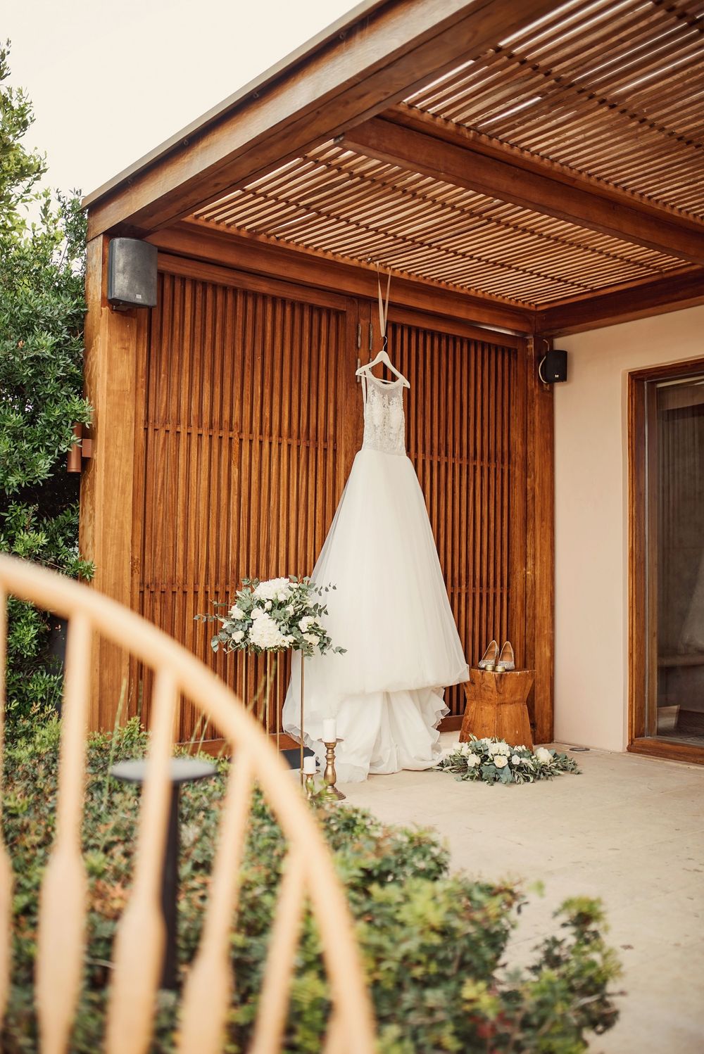 Classic white wedding gown displayed against wooden slatted wall under covered patio.