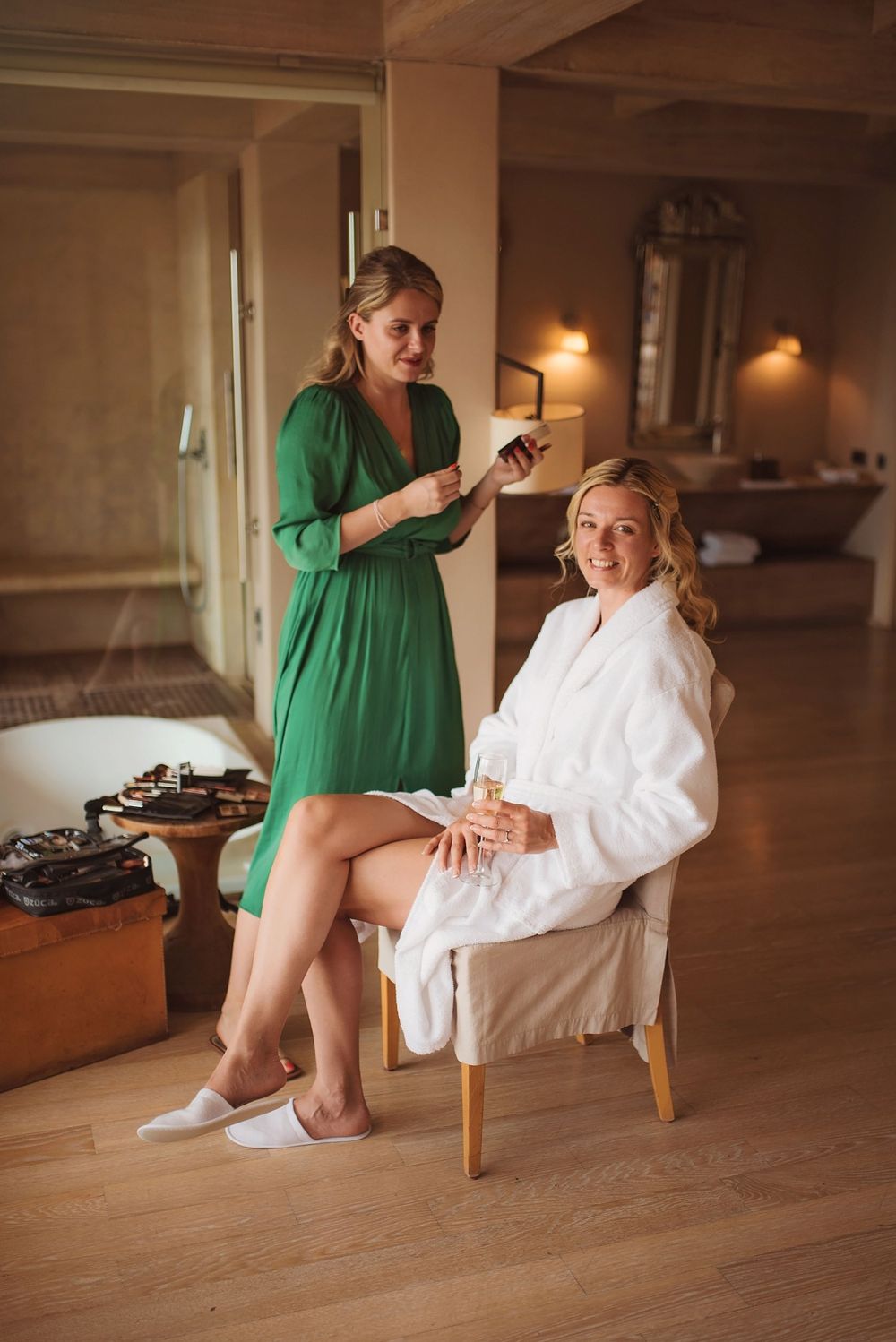 Two people share a candid moment during hair styling preparations in a warm-lit room.