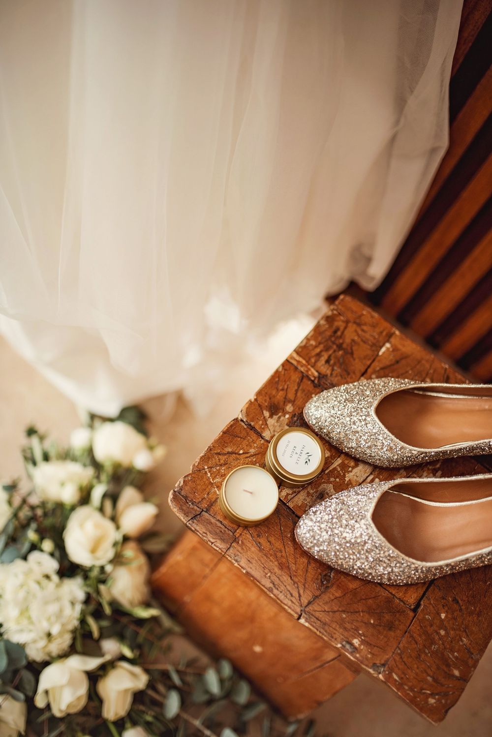 Silver glitter wedding flats on rustic wooden table with white roses and candles.