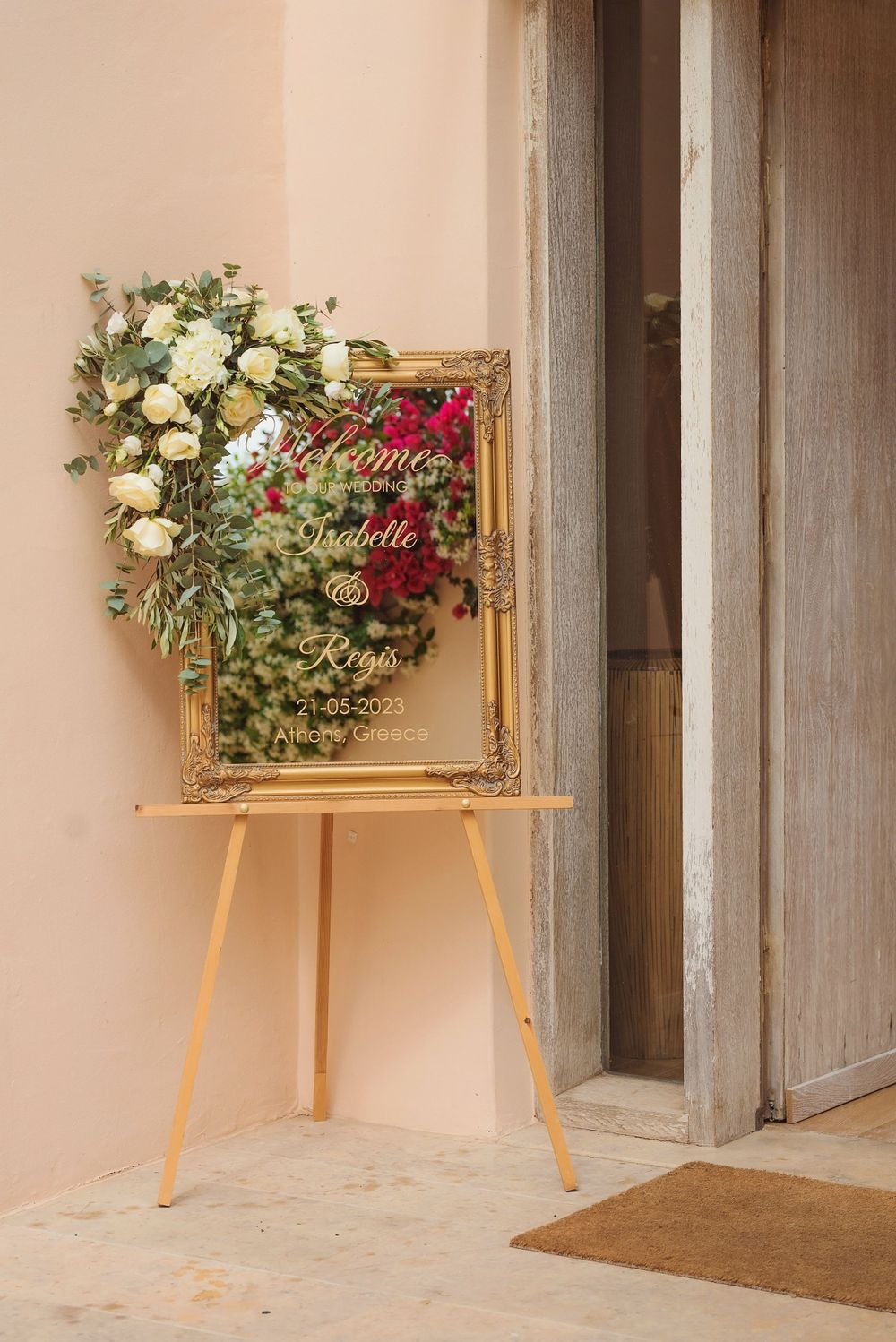 A decorative gold frame with white and red flowers on an easel near a doorway.