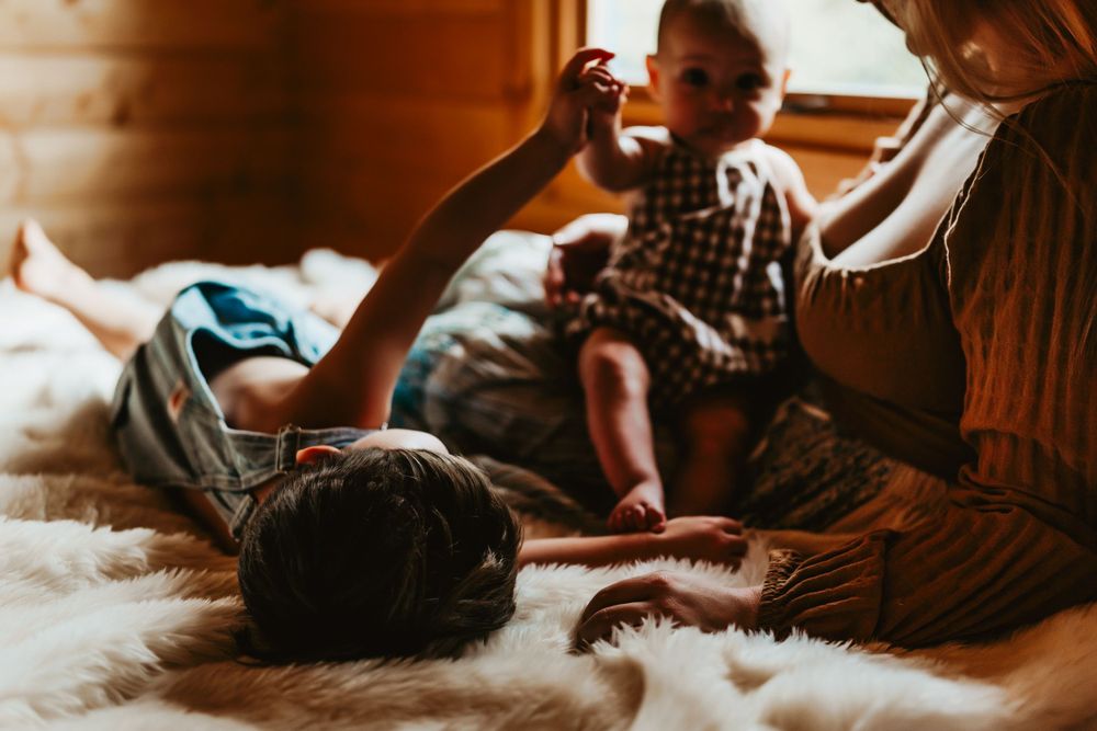 Warm sunlit scene of family bonding on soft bedding in a wooden cabin.