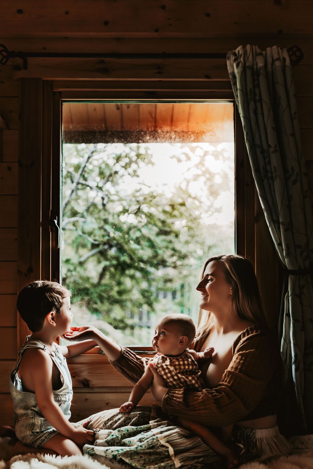 A cozy window scene inside a wooden cabin with warm sunlight streaming in during an intimate family moment.