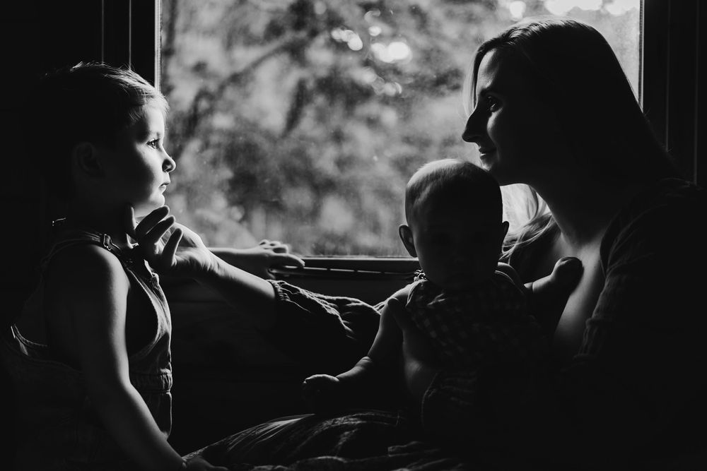 Silhouetted figures sitting together by a window in black and white.