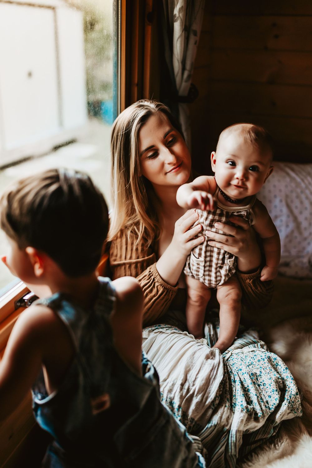 Tender family moment by a window in a rustic cabin with natural lighting and cozy bedding.