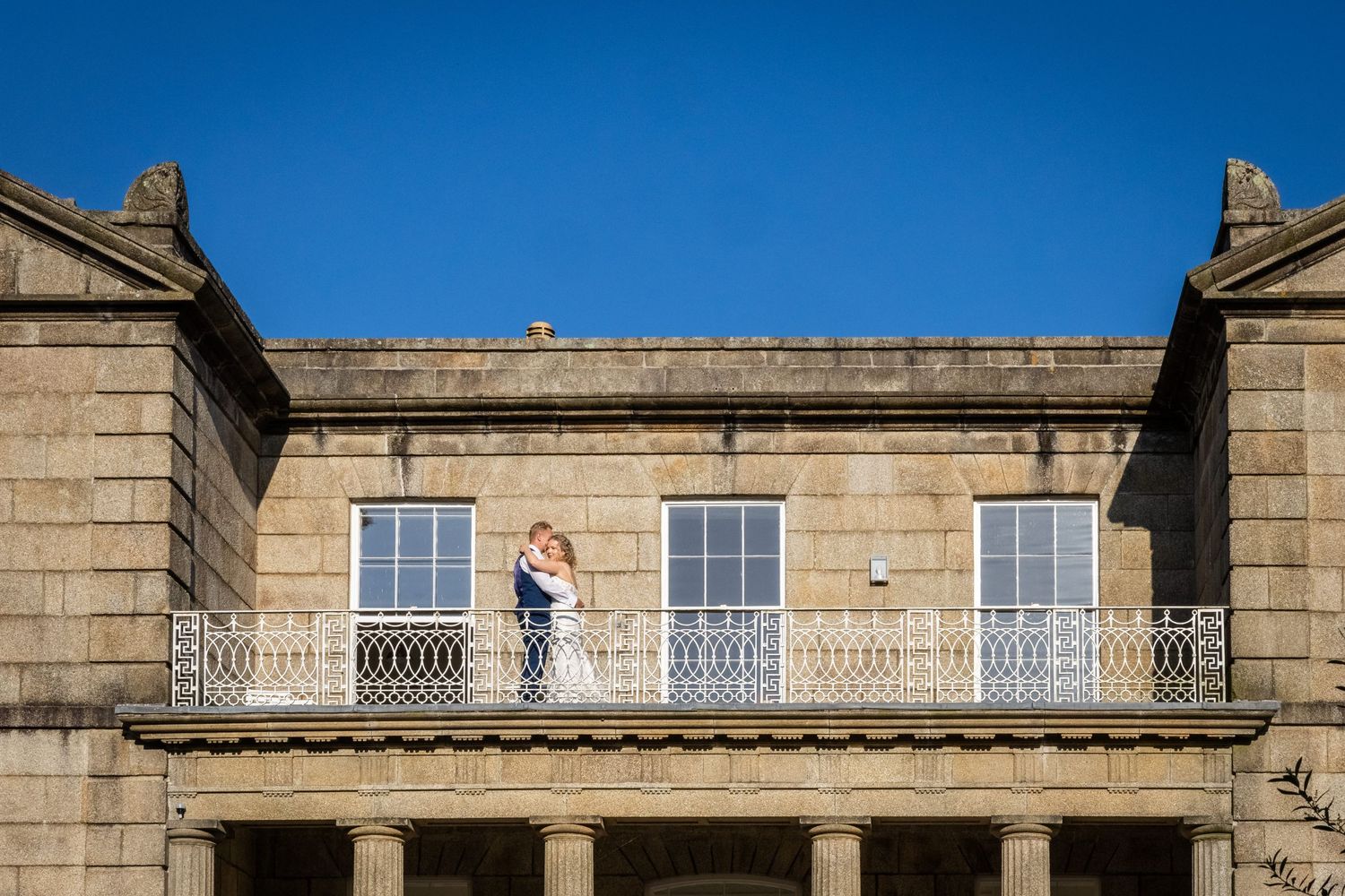 Historic stone building with ornate architectural details and windows against bright blue sky.