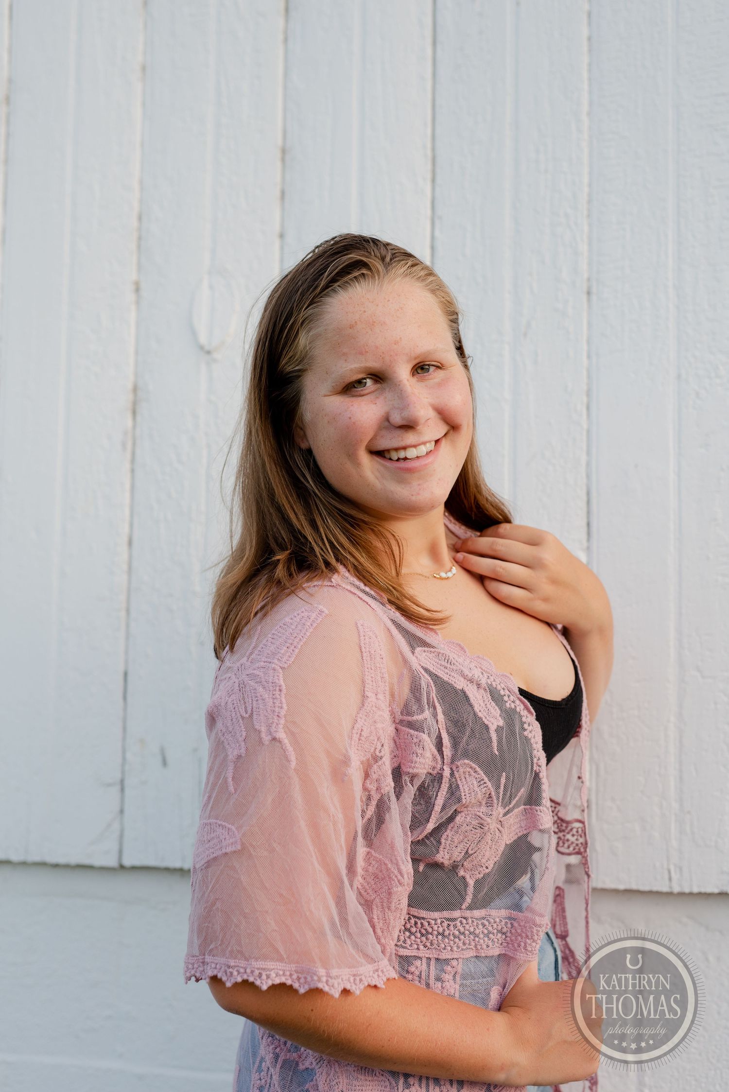 Someone in a pink lace top poses against a white wall during an outdoor photoshoot.