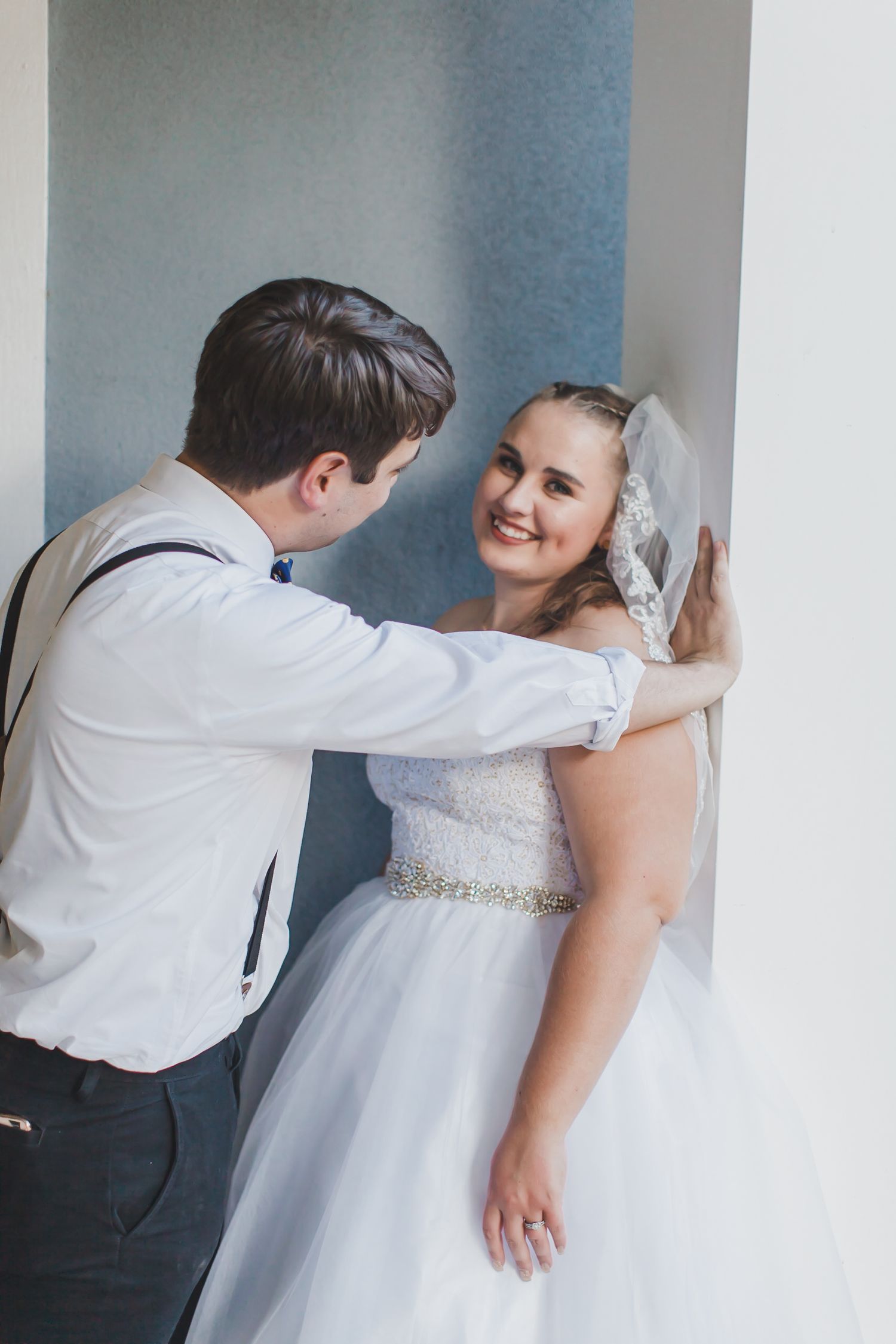 Wedding couple sharing a playful moment against a white wall background.