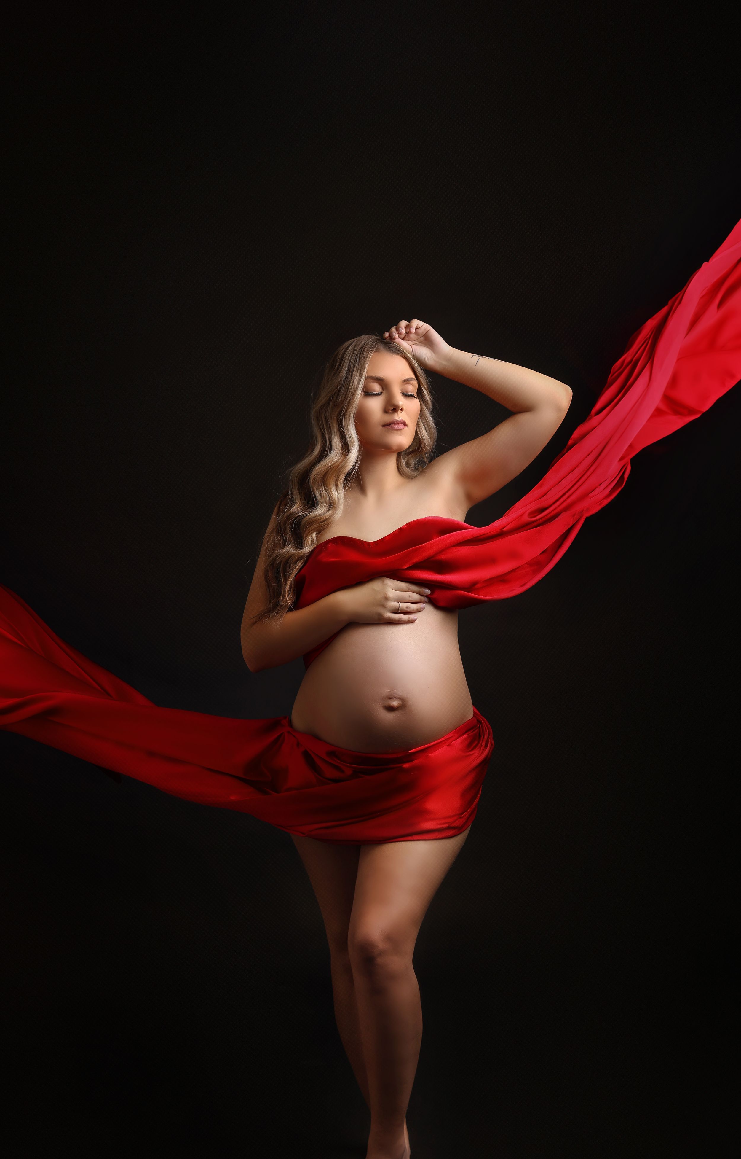 Dramatic maternity portrait with flowing red fabric against dark background.