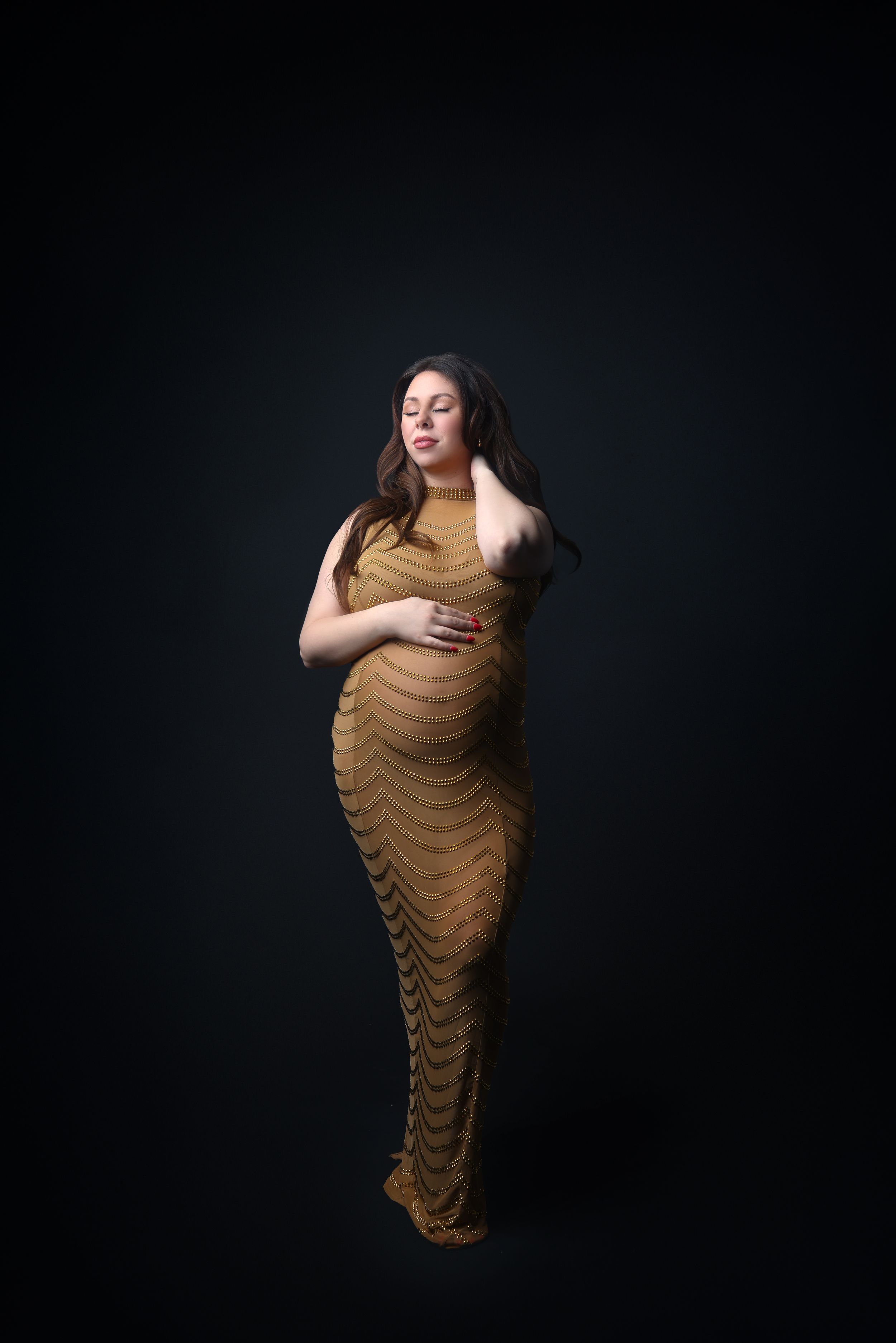 Artistic maternity portrait in fitted brown textured gown against dark background.