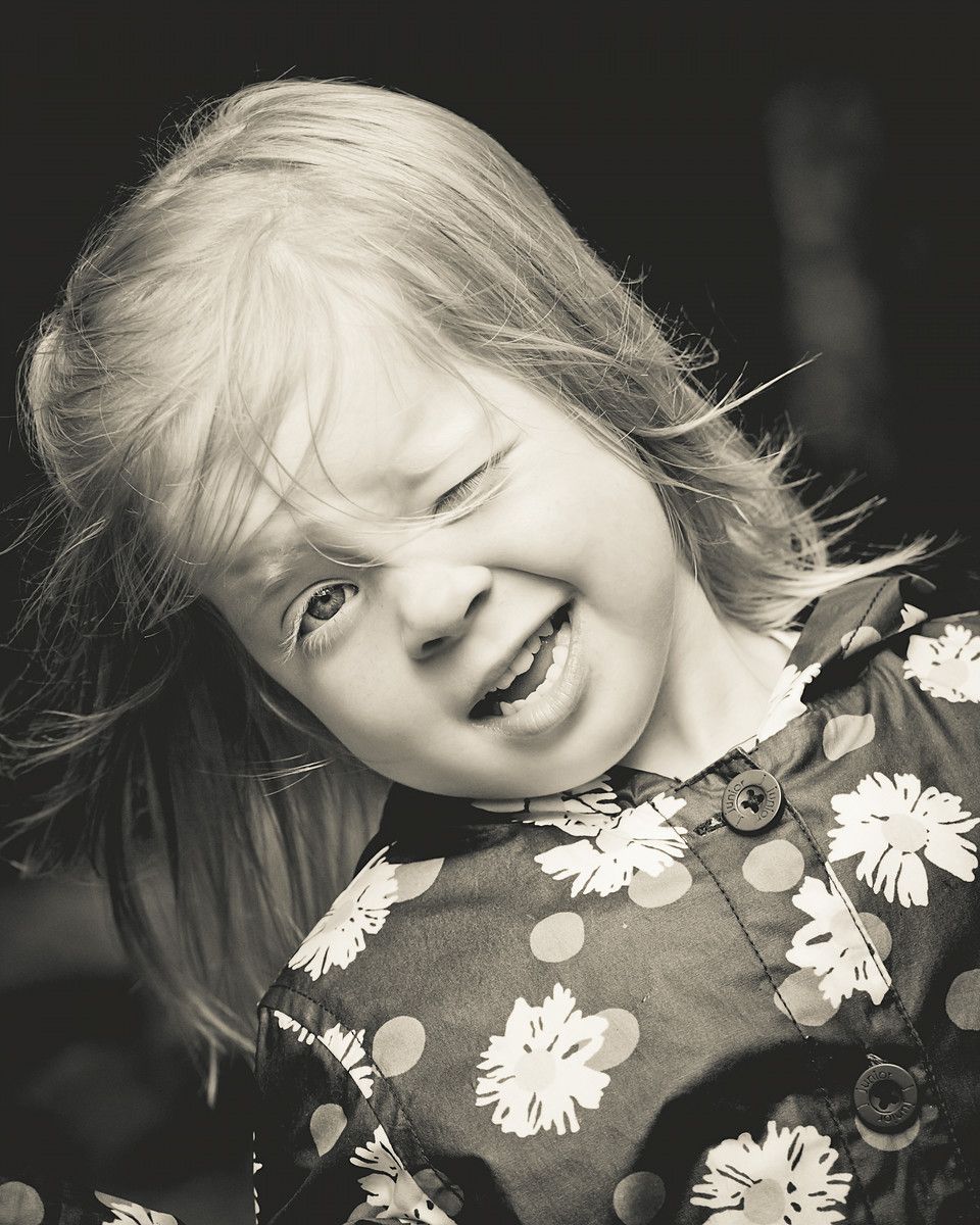 Black and white portrait of a joyful child wearing a floral dress.