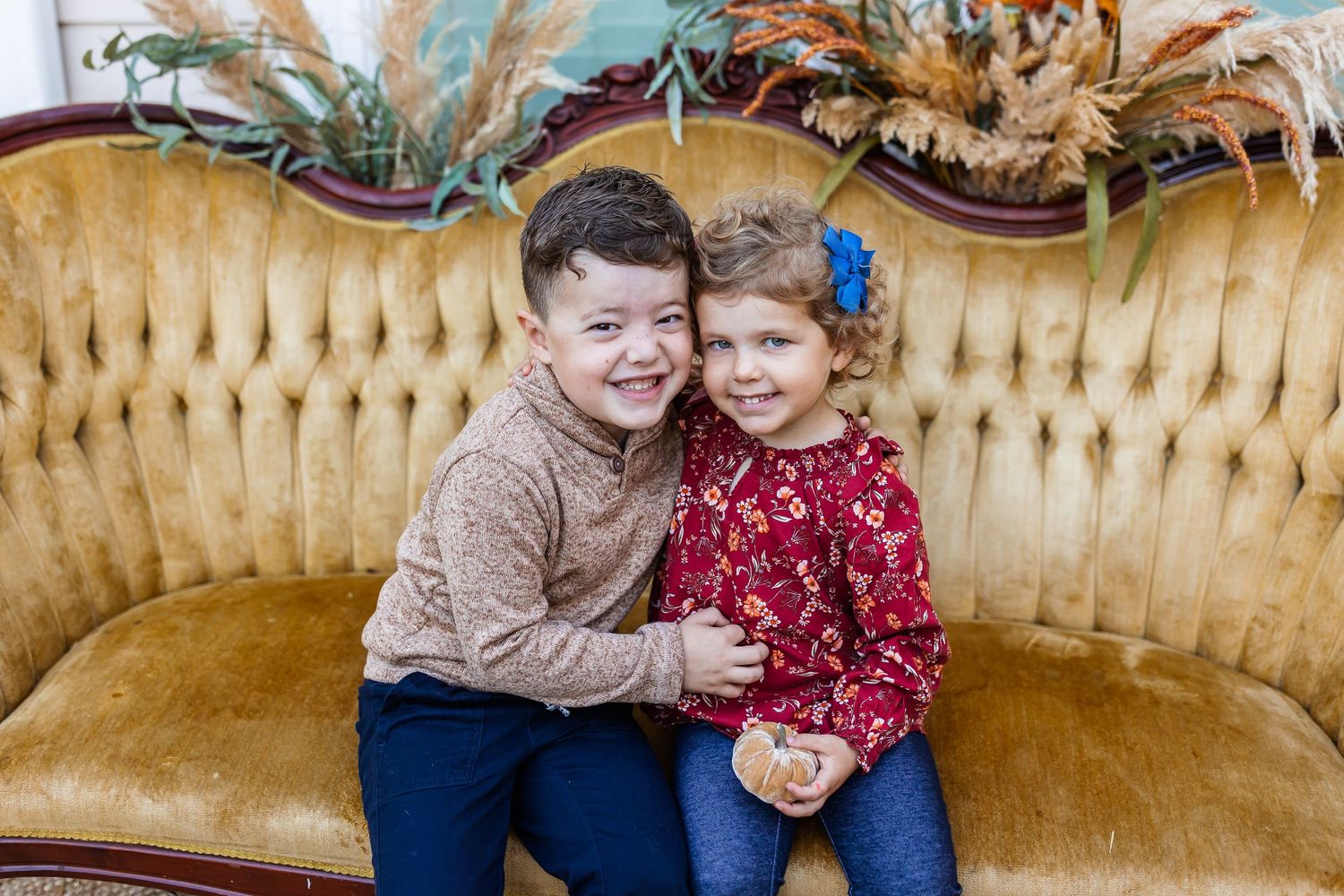 Children display affection while sitting together on an antique yellow velvet sofa.