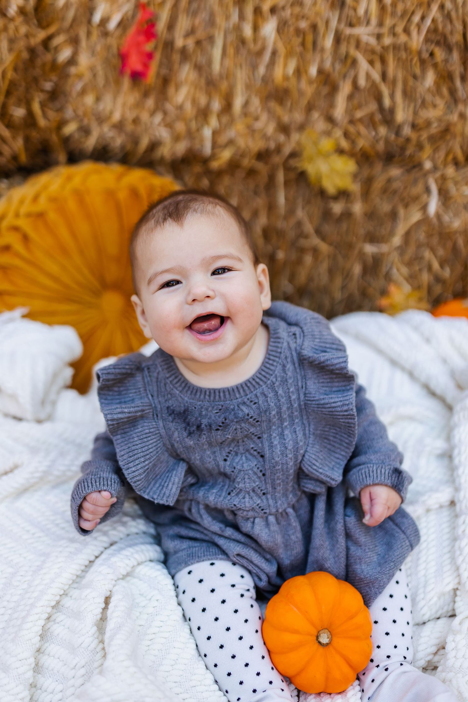Baby wearing knit sweater with small pumpkin on white blanket during fall photo session.