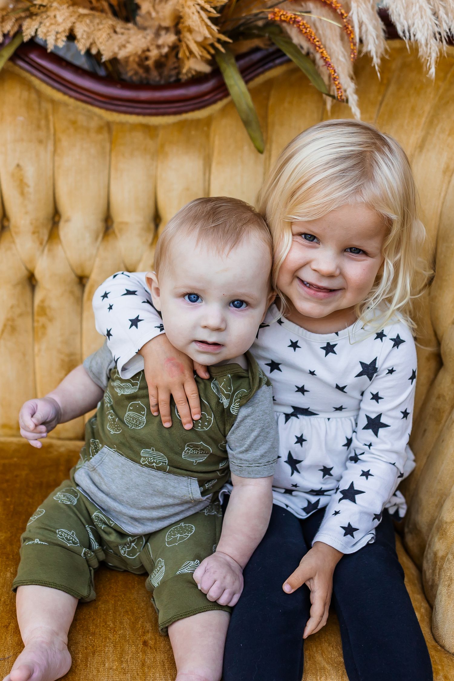 Two children in casual wear play and interact on a vintage yellow sofa.