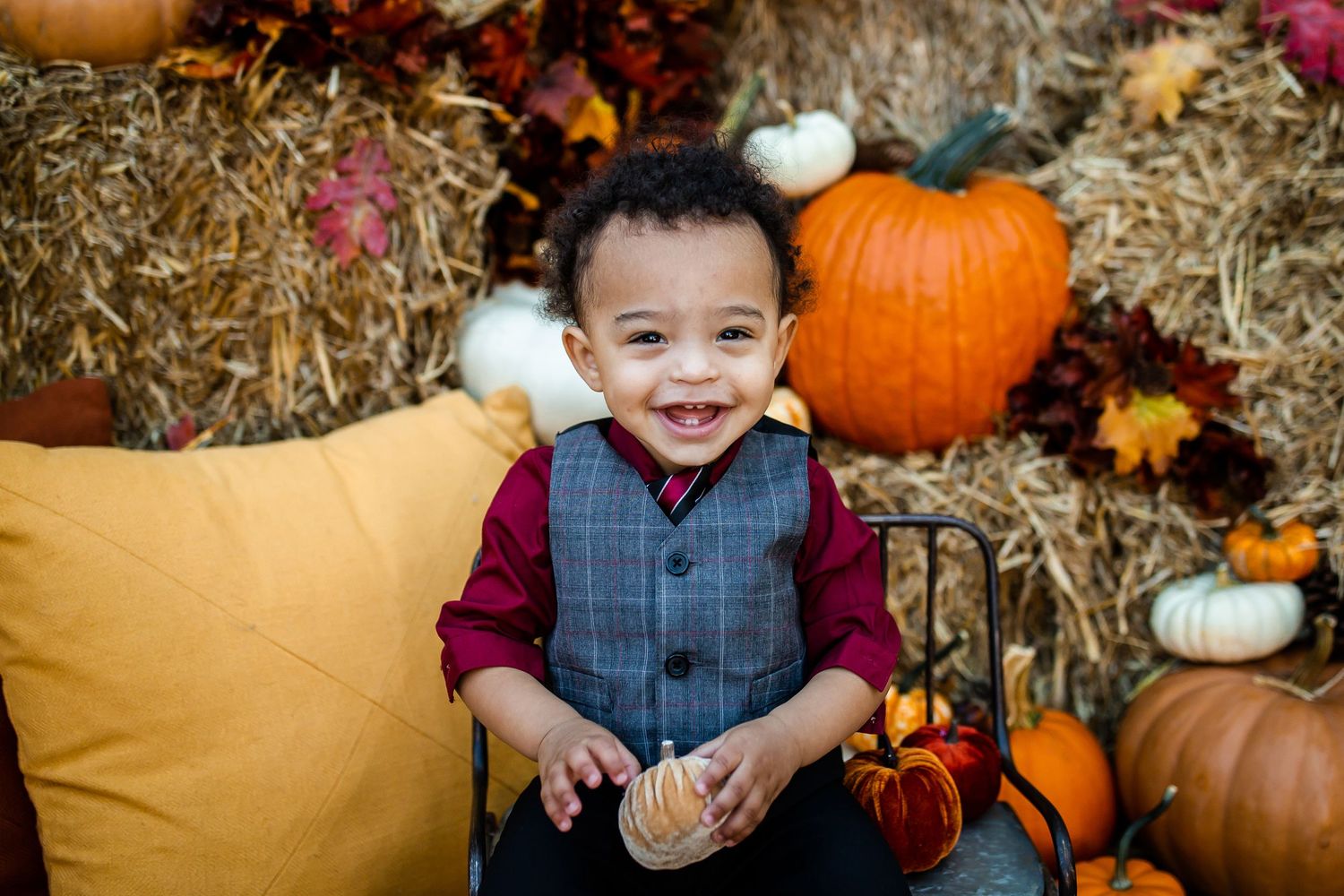Fall portrait with smiling child surrounded by pumpkins and hay bales.