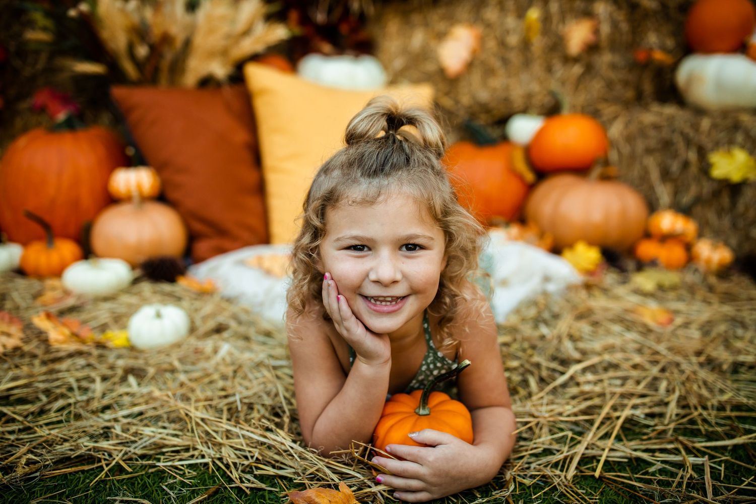 Cheerful autumn portrait amid orange pumpkins and hay with natural lighting.