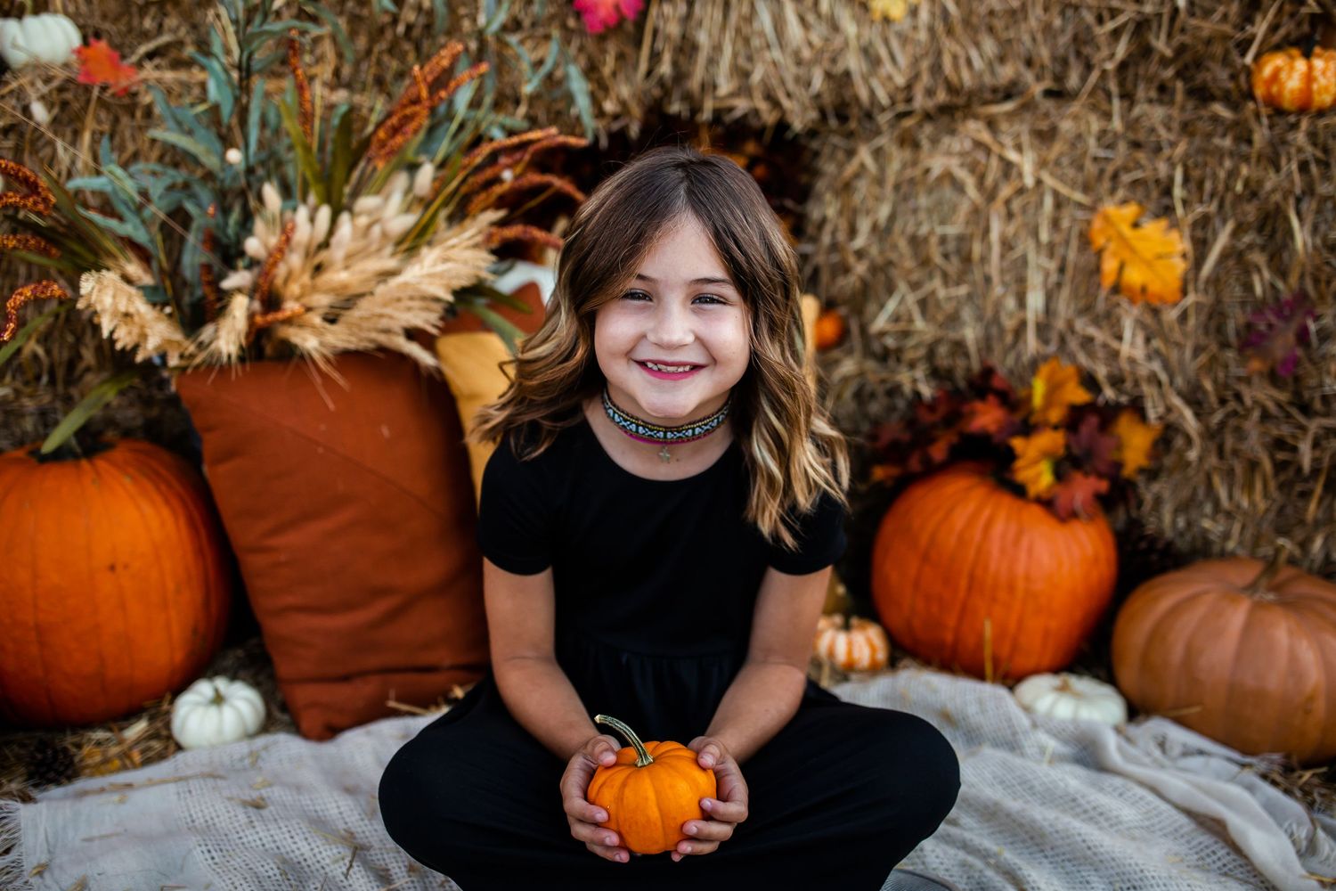 Autumn portrait with small orange pumpkin against hay bales and rustic backdrop.