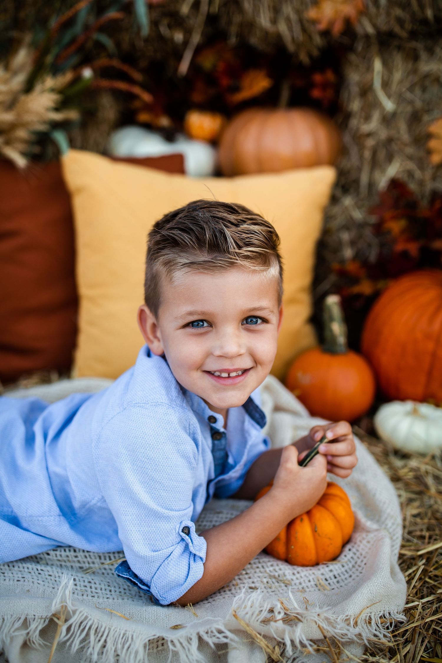 Fall portrait with pumpkins and hay bales featuring a casual blue button-down shirt.