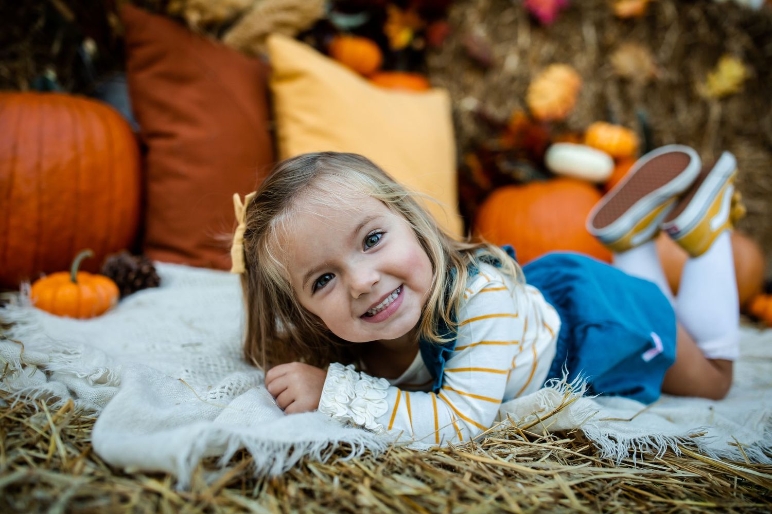 Autumn portrait session with orange pumpkins and hay bales in natural lighting.