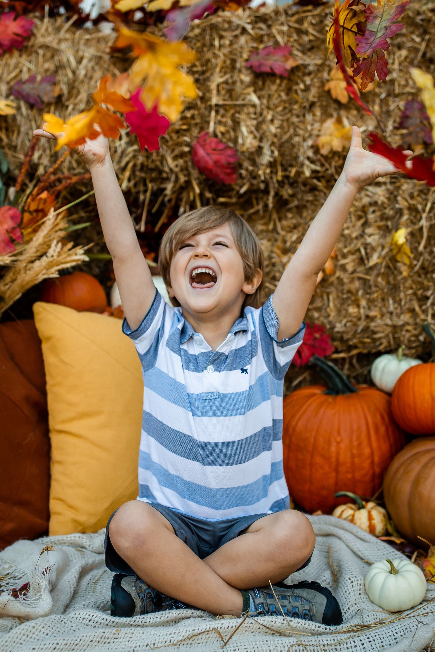 Pure joy captured during autumn with raised arms against a backdrop of fall leaves and pumpkins.