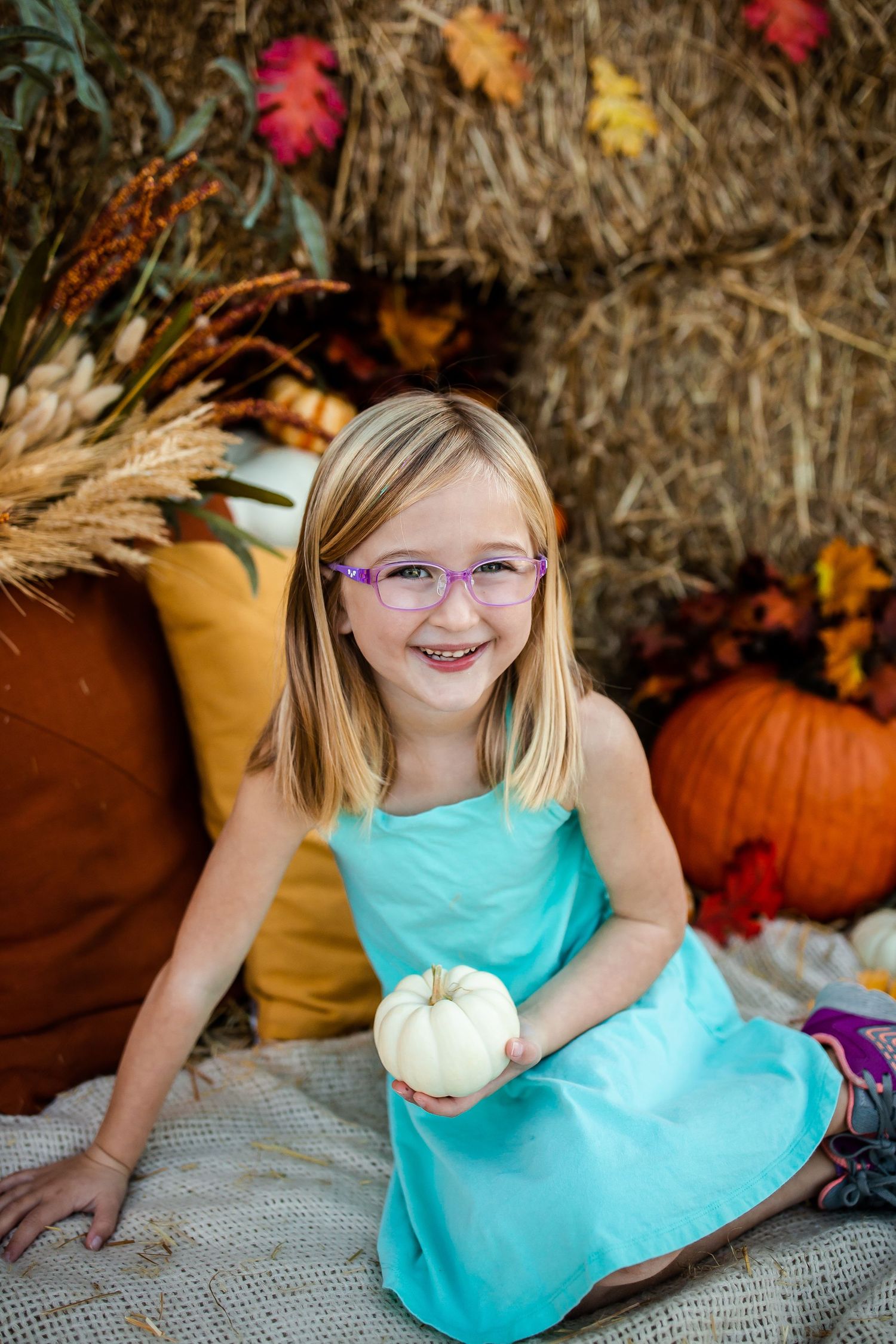 Cheerful autumn scene with turquoise dress against colorful fall leaves and pumpkin decorations.