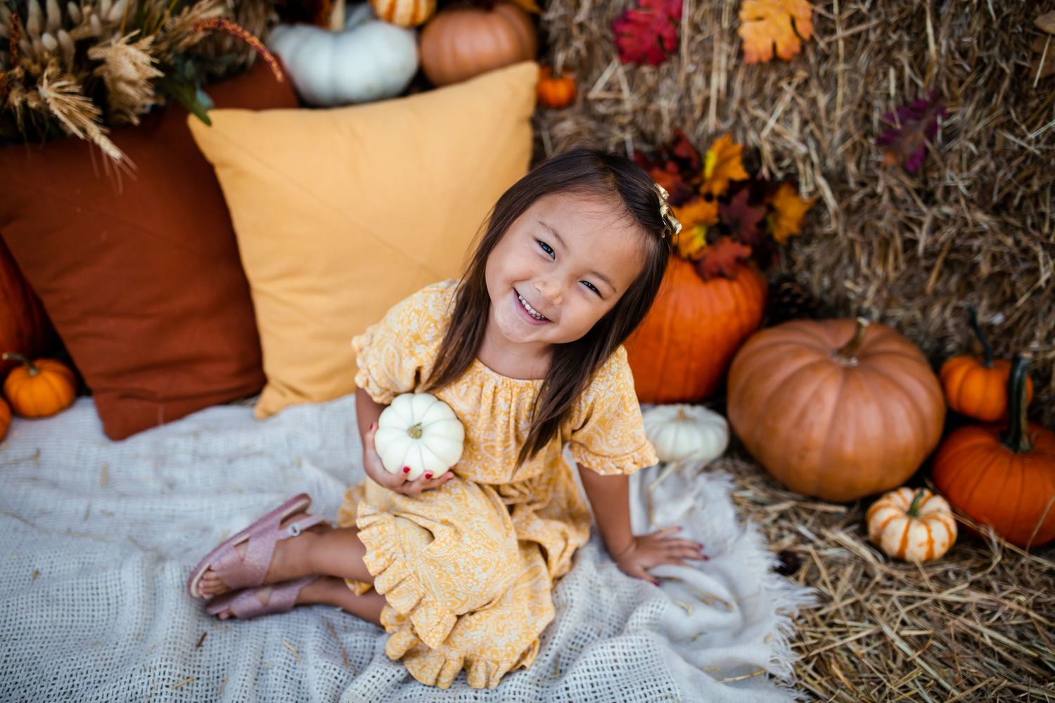 Candid autumn photo shoot with decorative pumpkins and hay bales in the background.