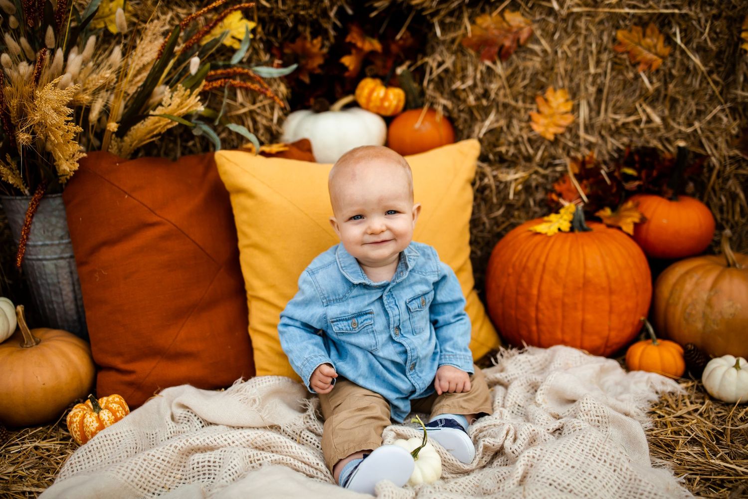 Fall harvest scene with cozy blankets, decorative pumpkins, yellow throw pillows and autumn decor on hay bales.