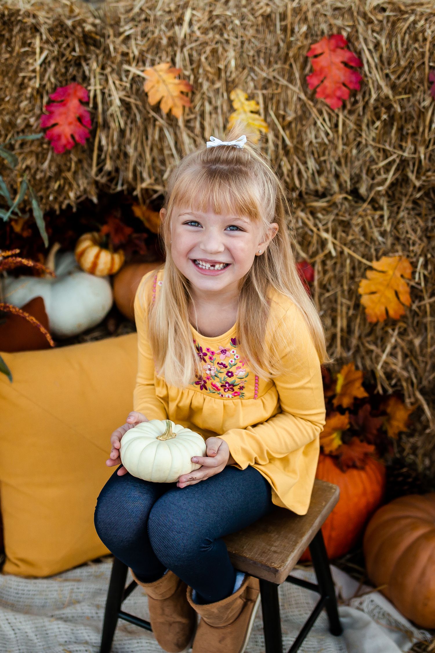 Autumn photo session with yellow sweater and white pumpkins on rustic bench.