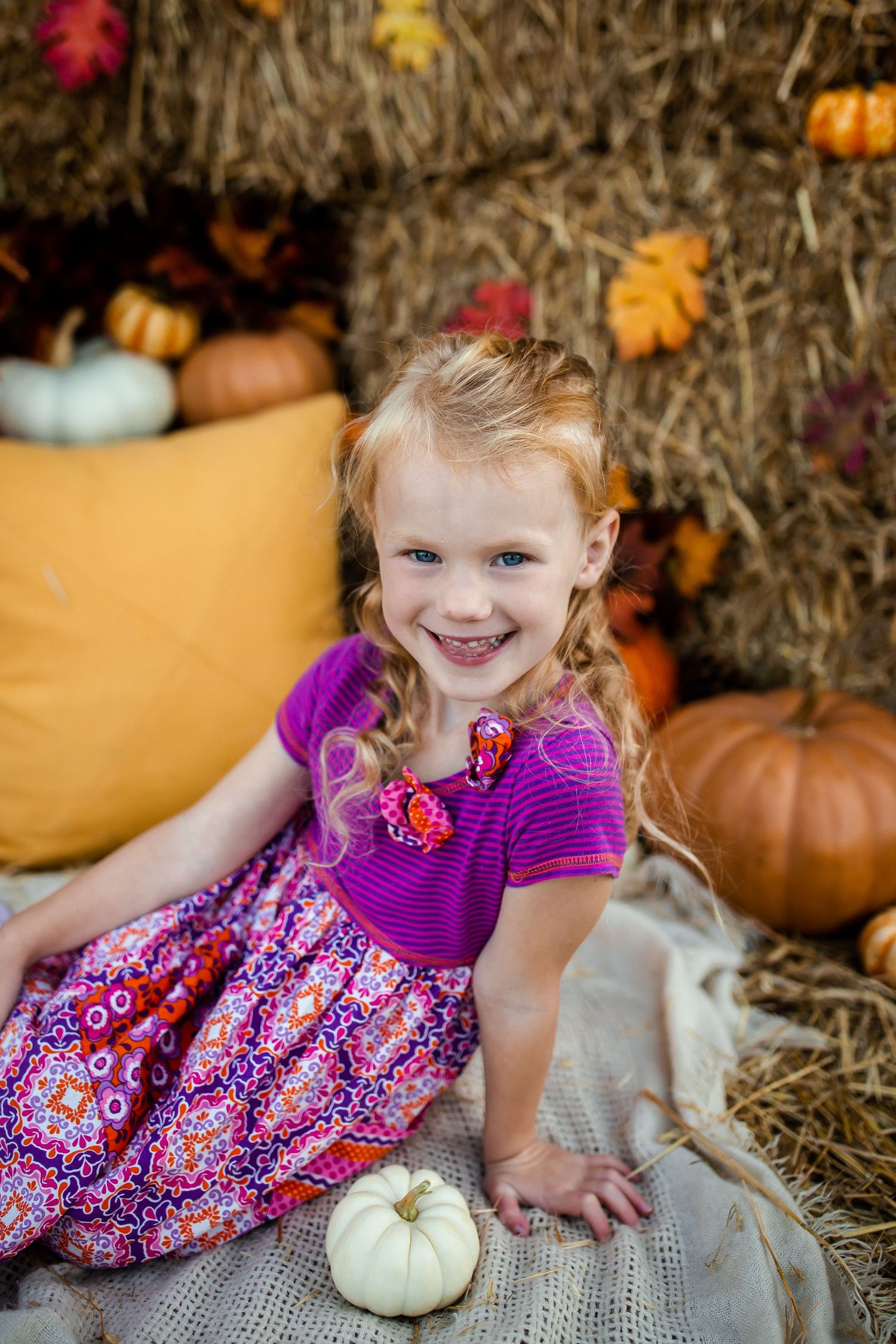 Festive fall portrait surrounded by pumpkins and colorful autumn decorations on hay bales.