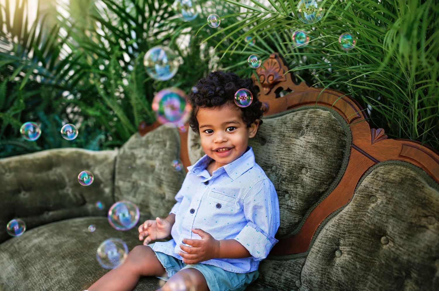 Child in blue shirt sitting on vintage couch with soap bubbles floating around.