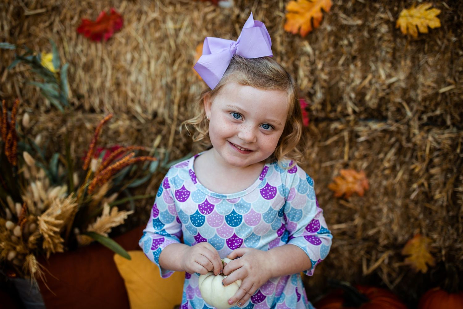 Sweet portrait of young girl in floral dress at autumn pumpkin patch display.