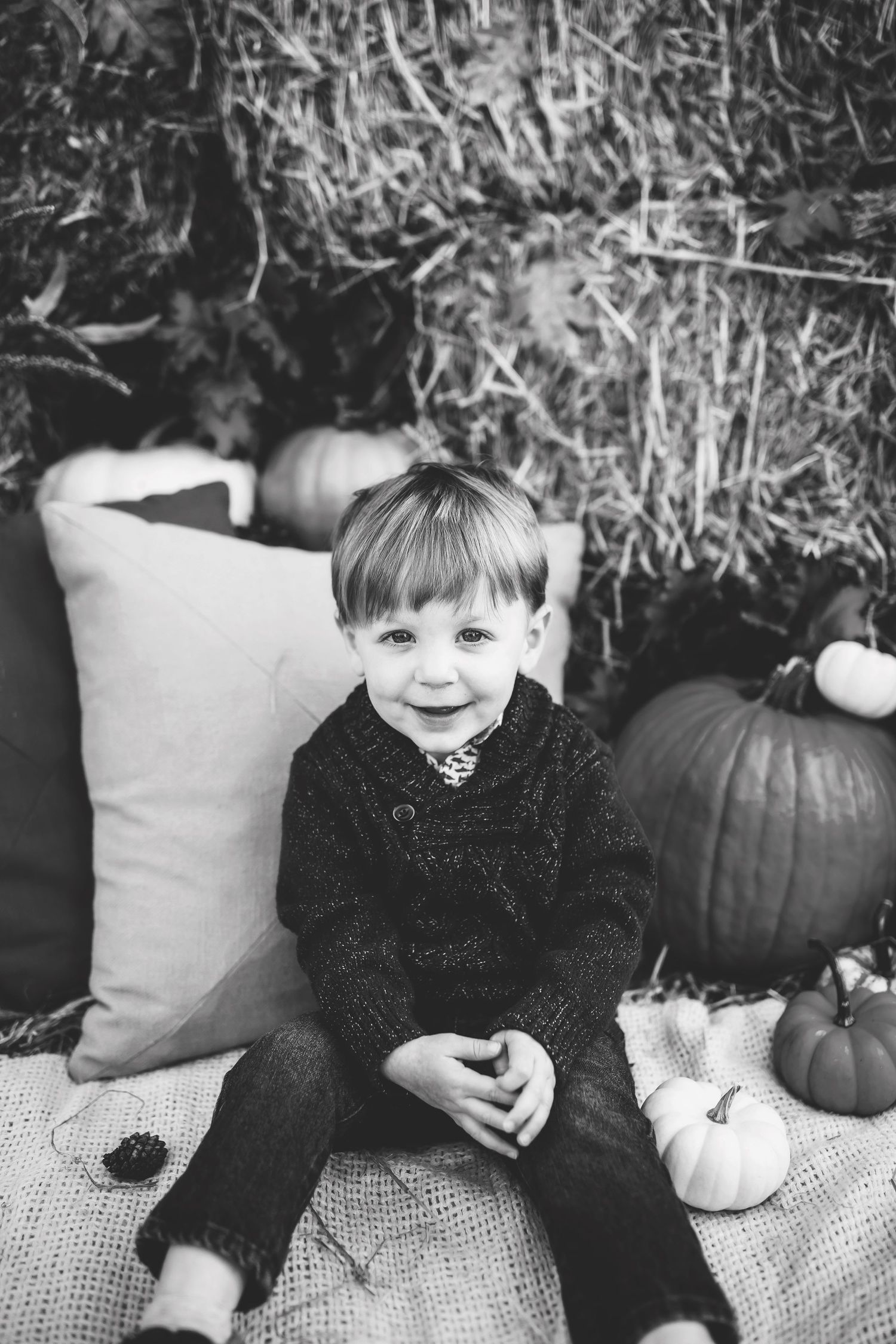 Black and white autumn portrait with decorative pumpkins and soft cushions on hay bales.