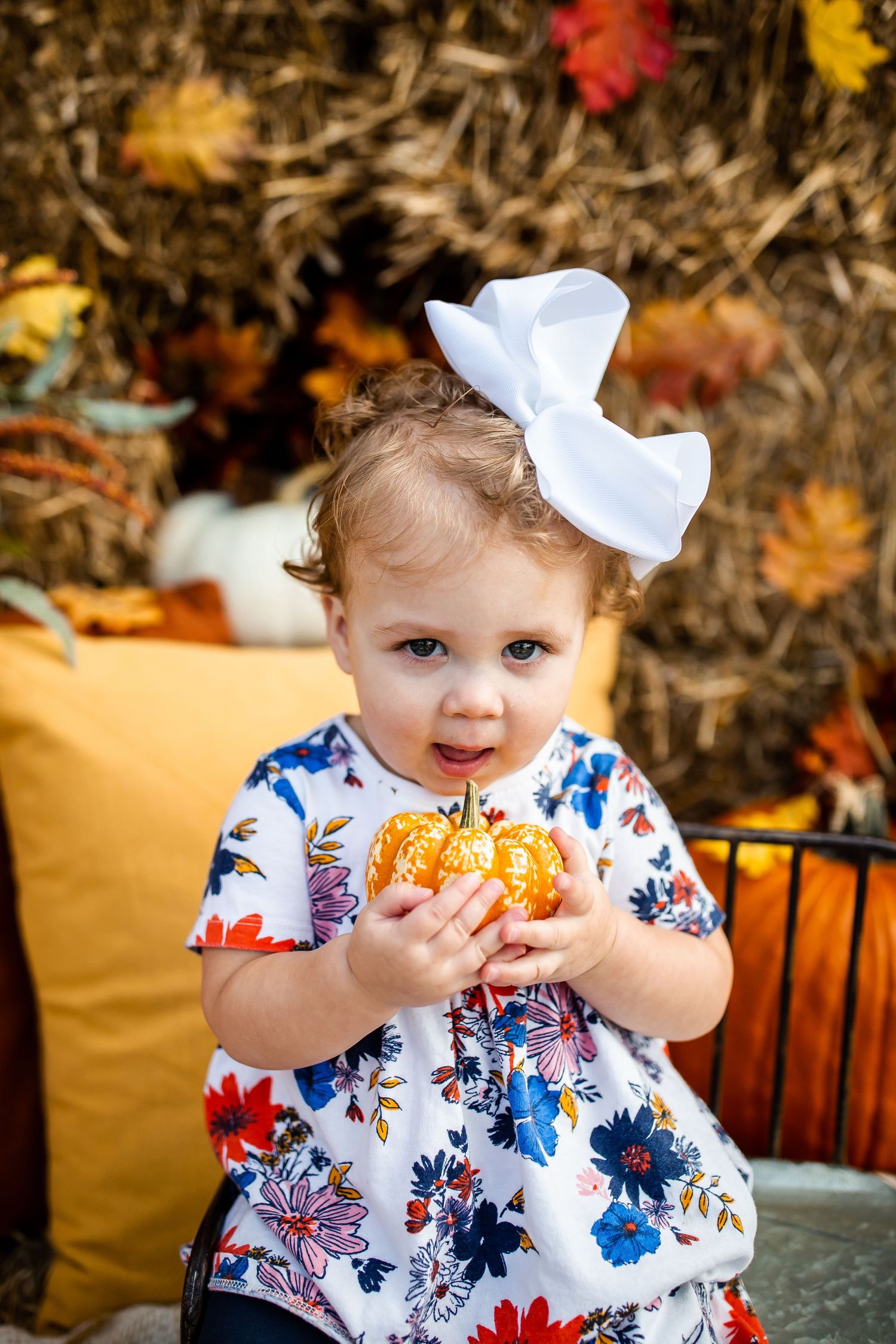 A sweet autumn portrait with pumpkins and colorful fall foliage in the background.