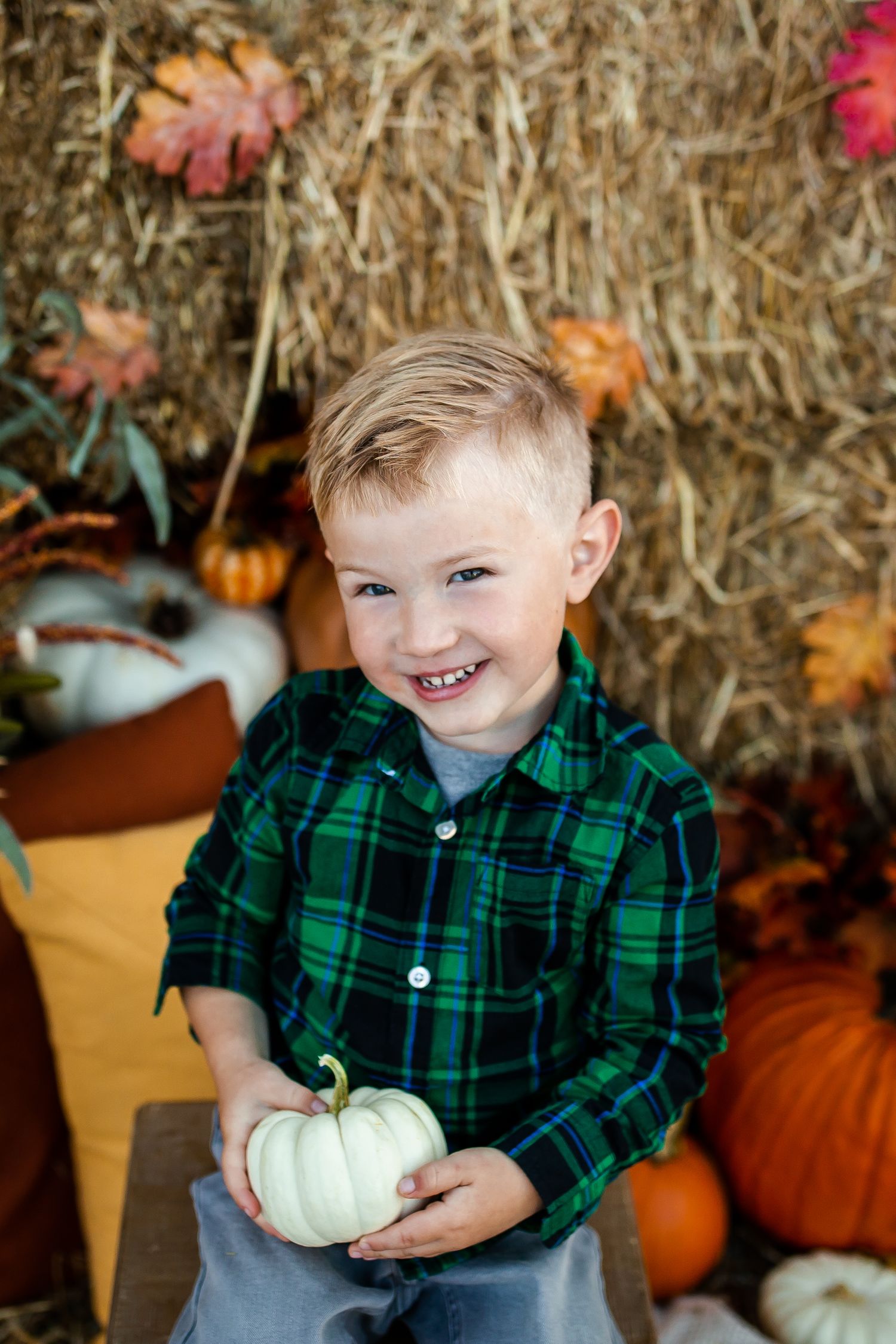 Fall portrait with pumpkins and hay bales featuring green plaid shirt.