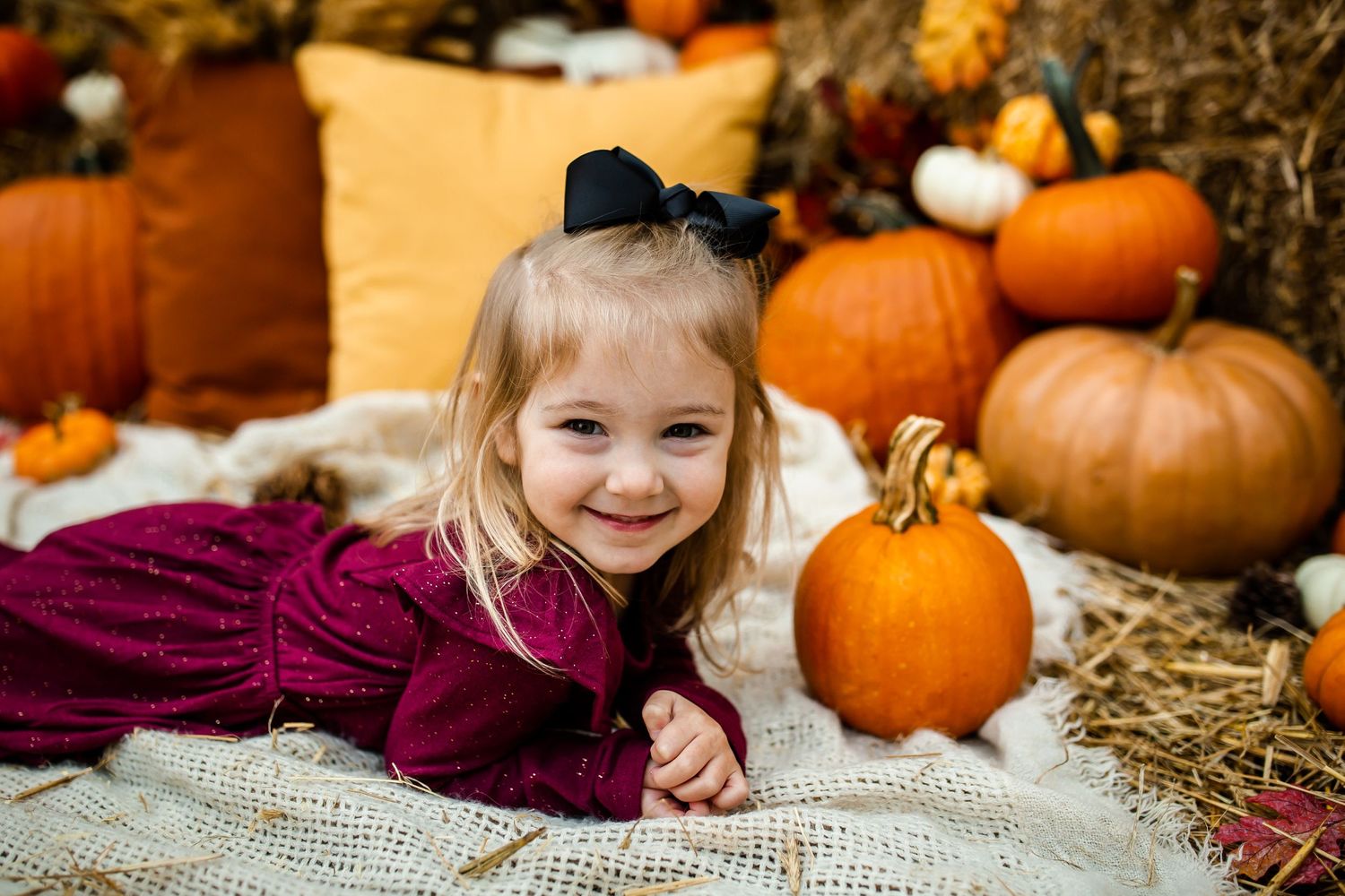 Cozy fall portrait with burgundy sweater against orange pumpkins and hay background.