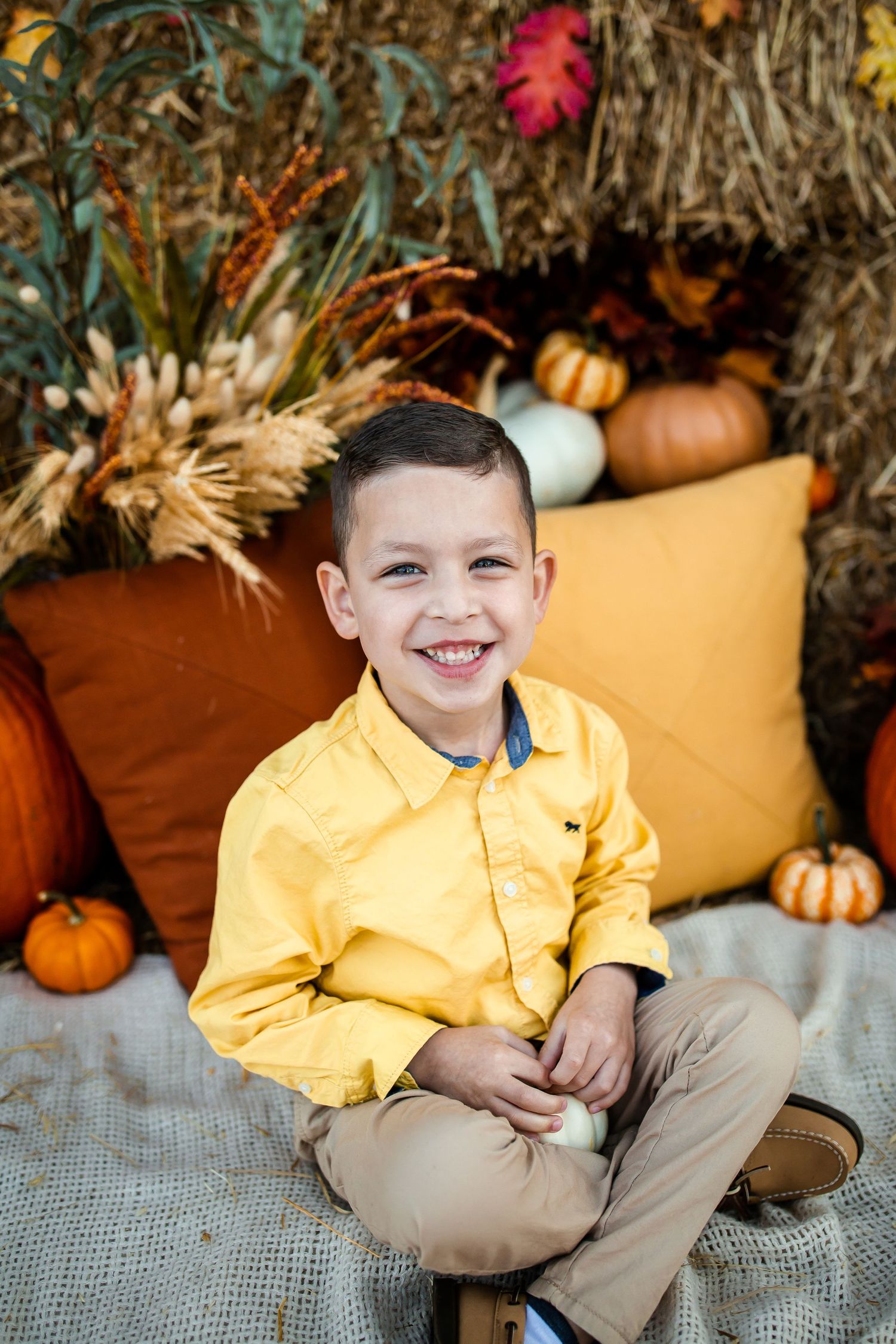 Autumn portrait session with yellow shirt against hay bale and pumpkin backdrop.