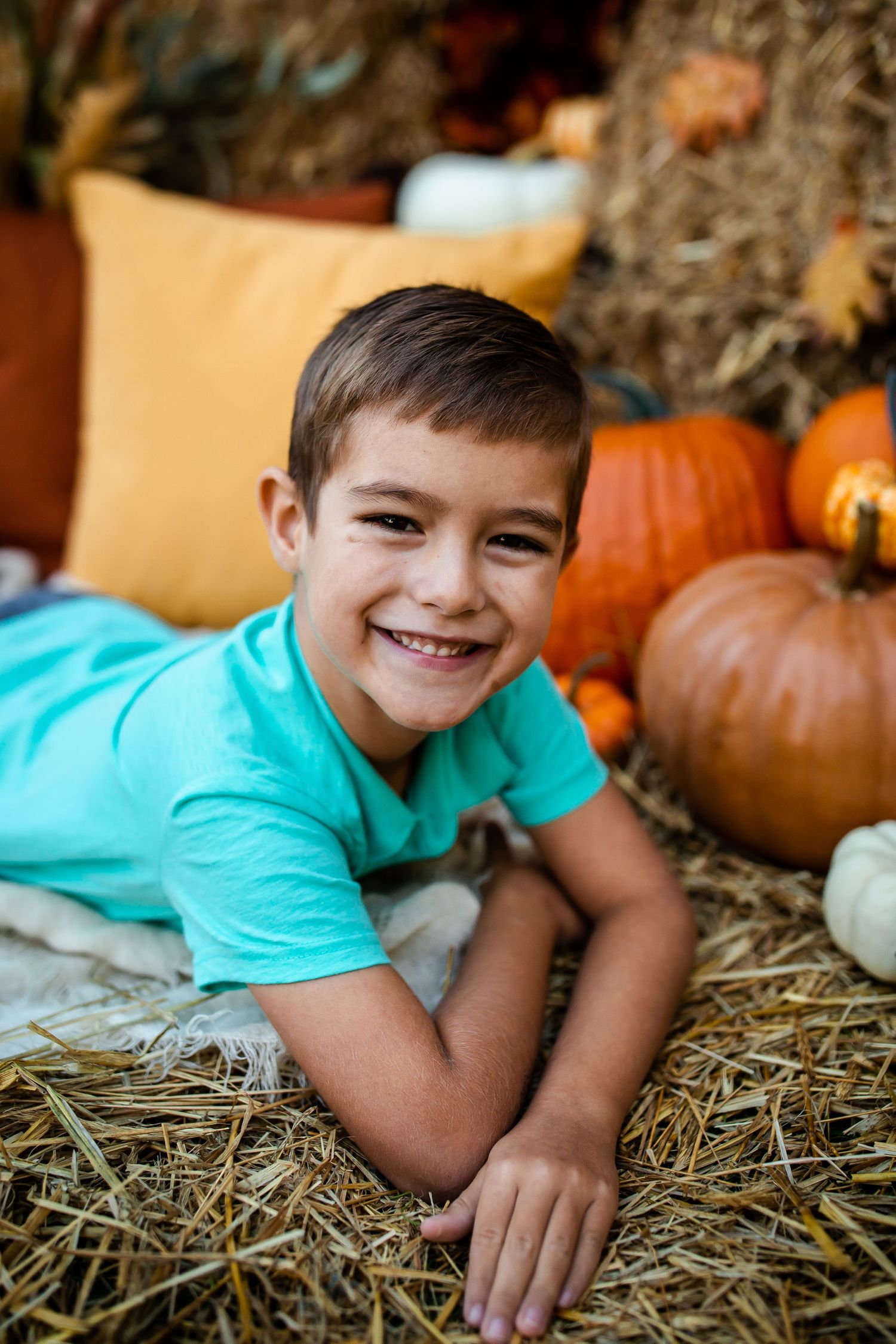Cozy autumn photo setup with teal shirt against hay bales and orange pumpkins.