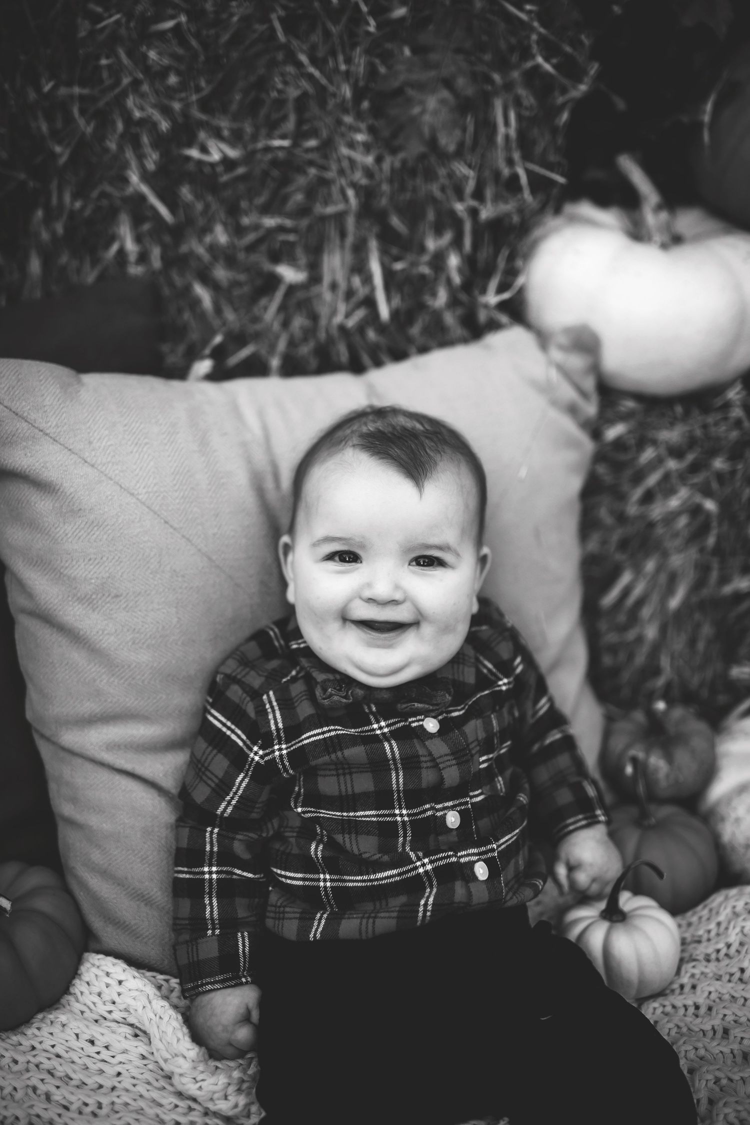 Black and white portrait with plaid shirt amid autumn pumpkin decorations.