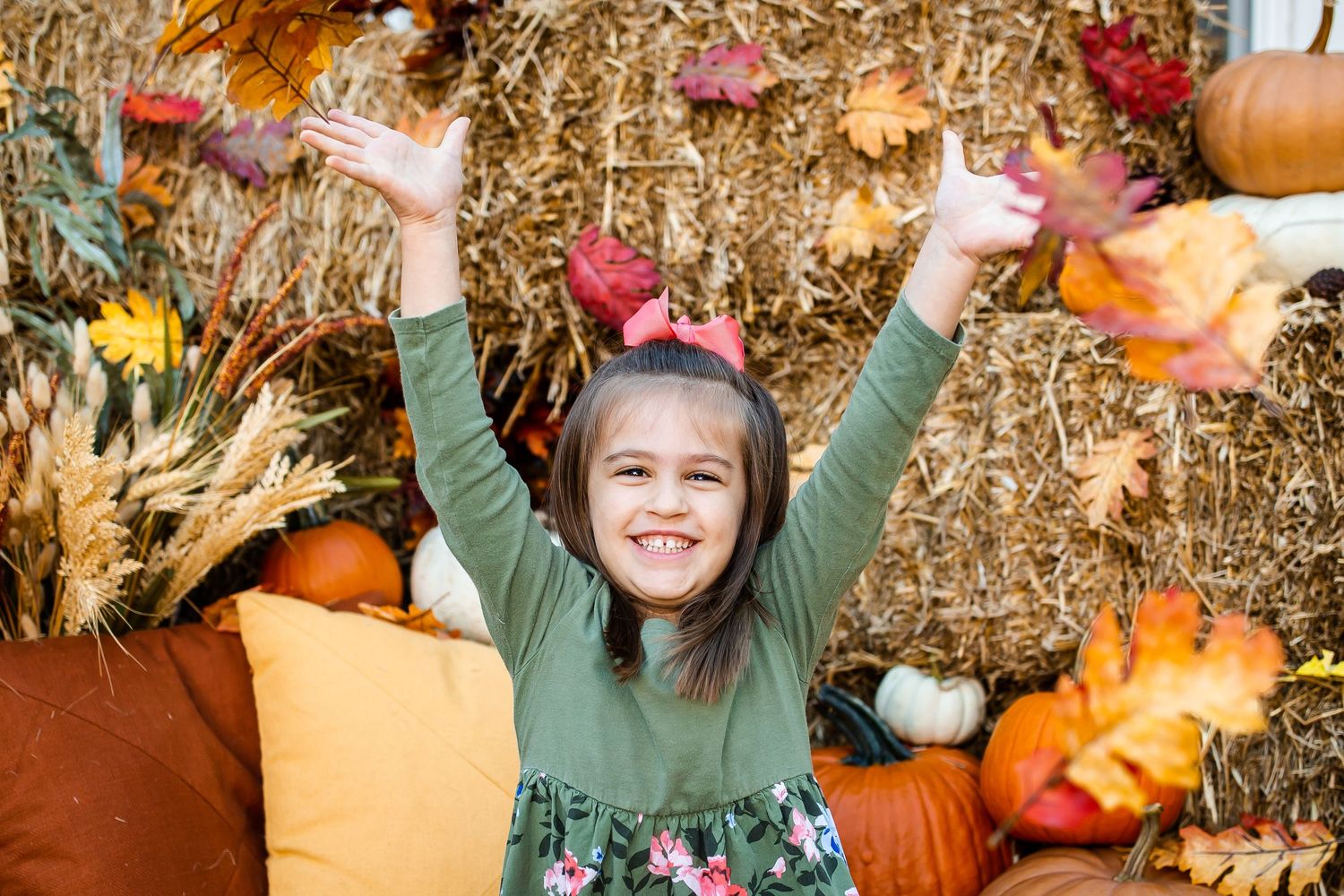Joyful child throwing autumn leaves at rustic fall themed photo setup.