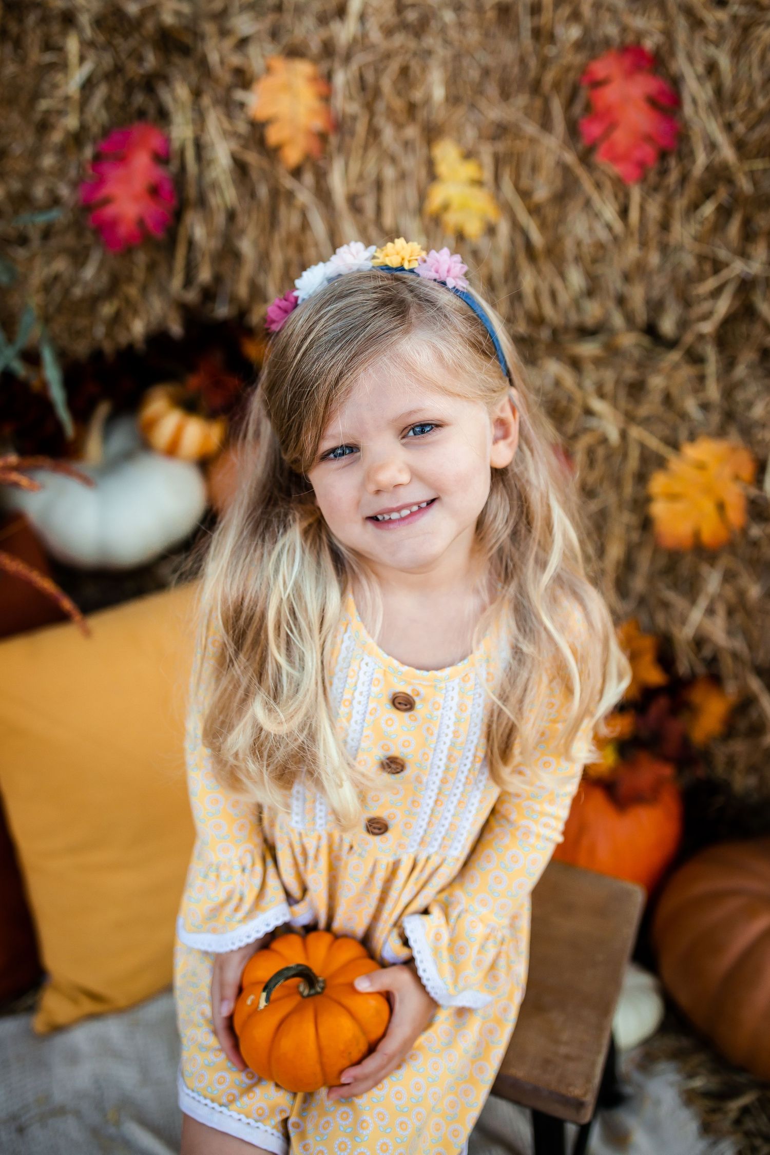 Autumn portrait with decorative pumpkins and colorful fall leaves against hay bale background.