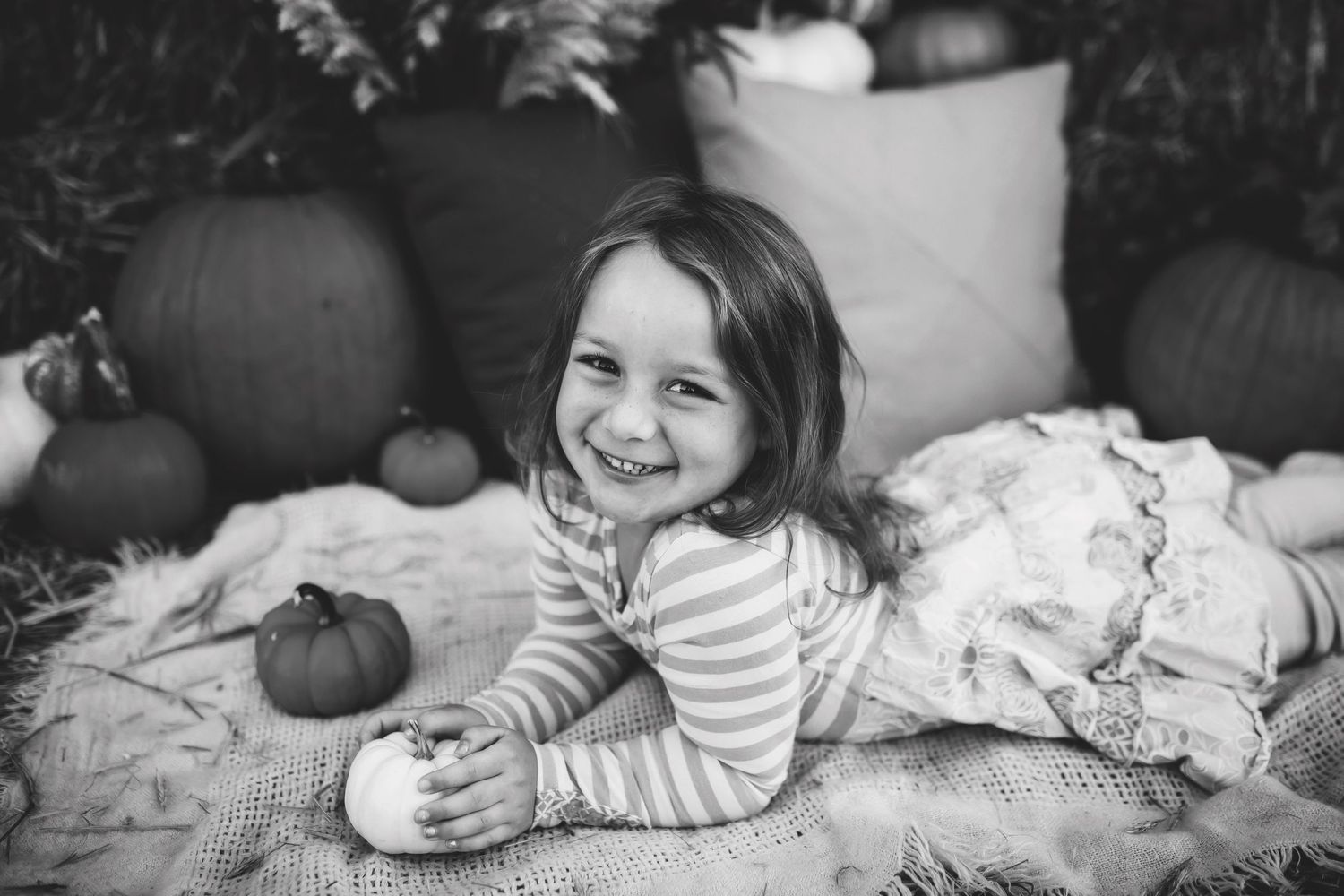 Cozy autumn family photoshoot with pumpkins and blankets in natural setting.