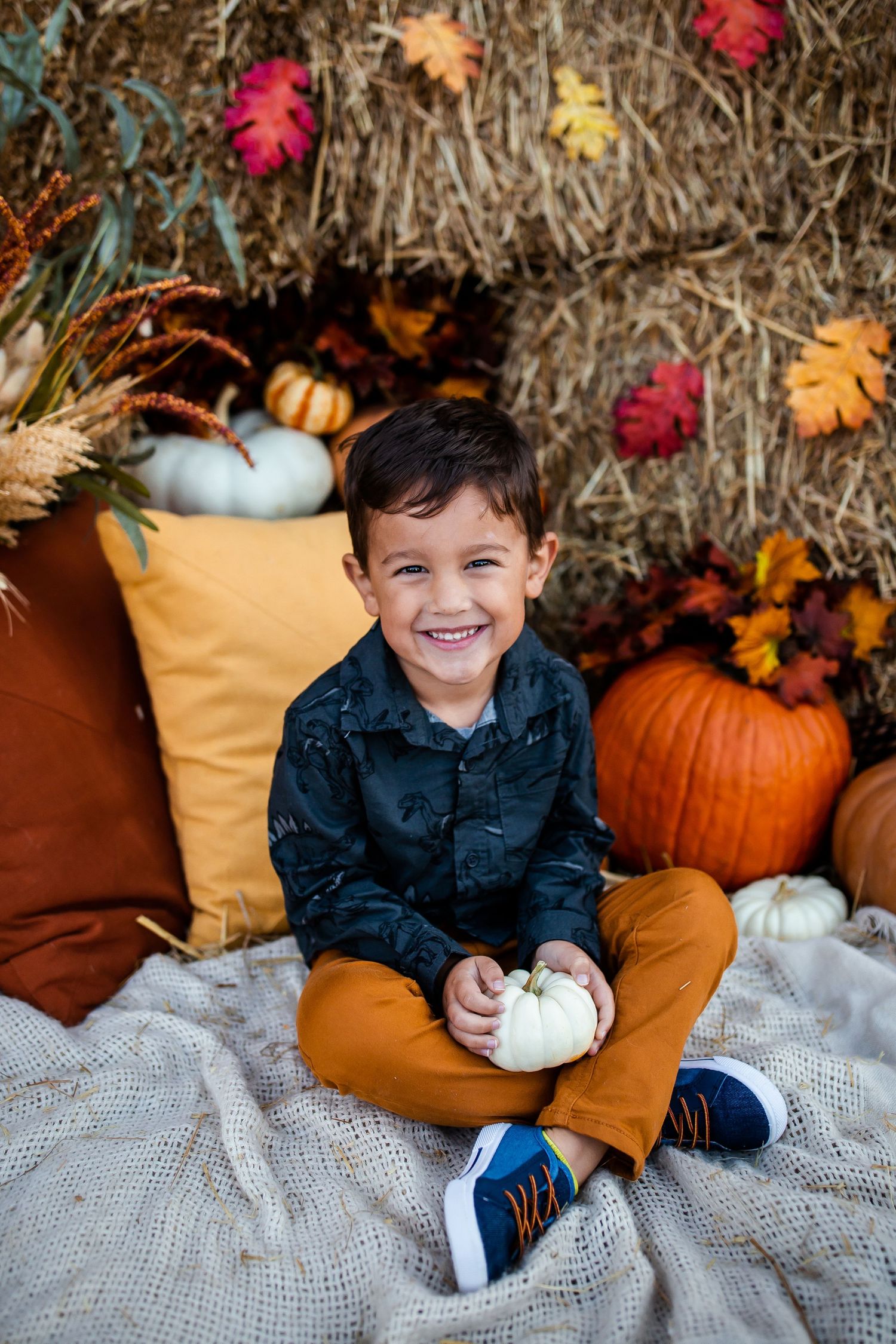 Festive fall scene with orange cushions, pumpkins and colorful autumn leaves on hay bales.