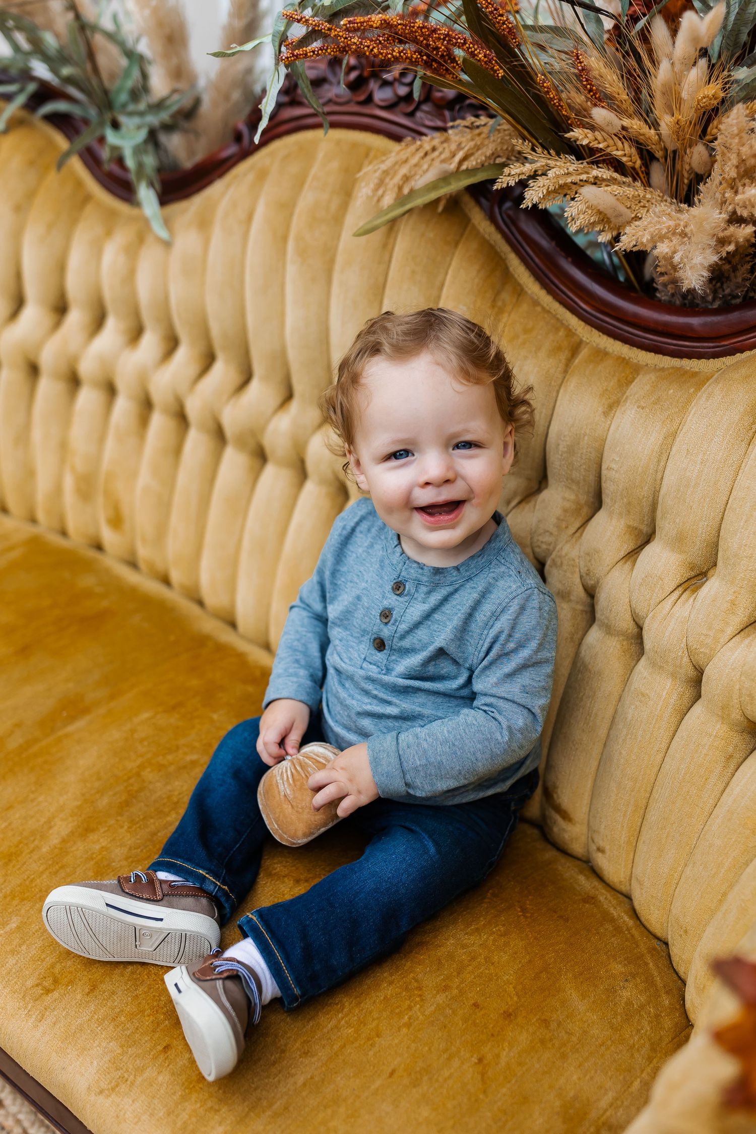 A young child wearing blue sits on a plush yellow vintage couch.