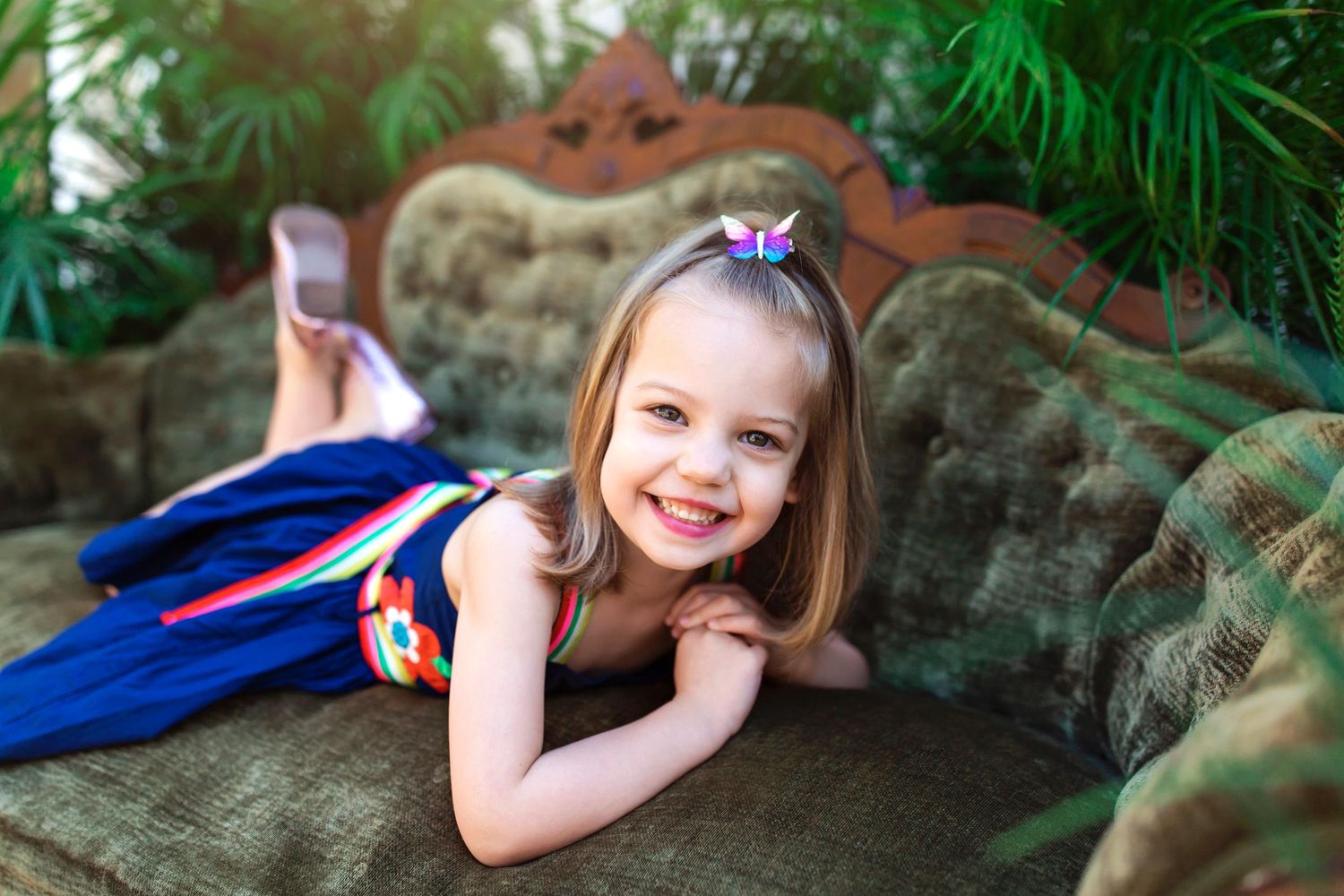Outdoor photo shoot with green palm fronds and a classic tufted couch.